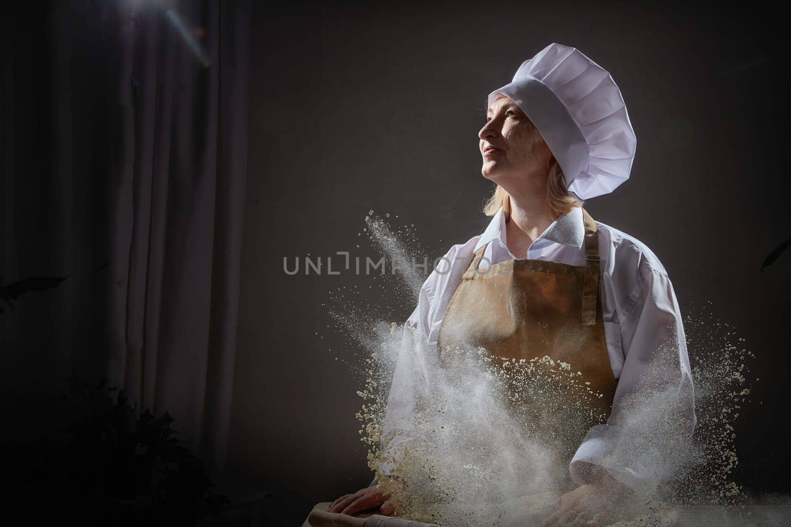 An elderly woman dressed as a cook happily interacts with flour while enjoying a humorous moment in the kitchen.
