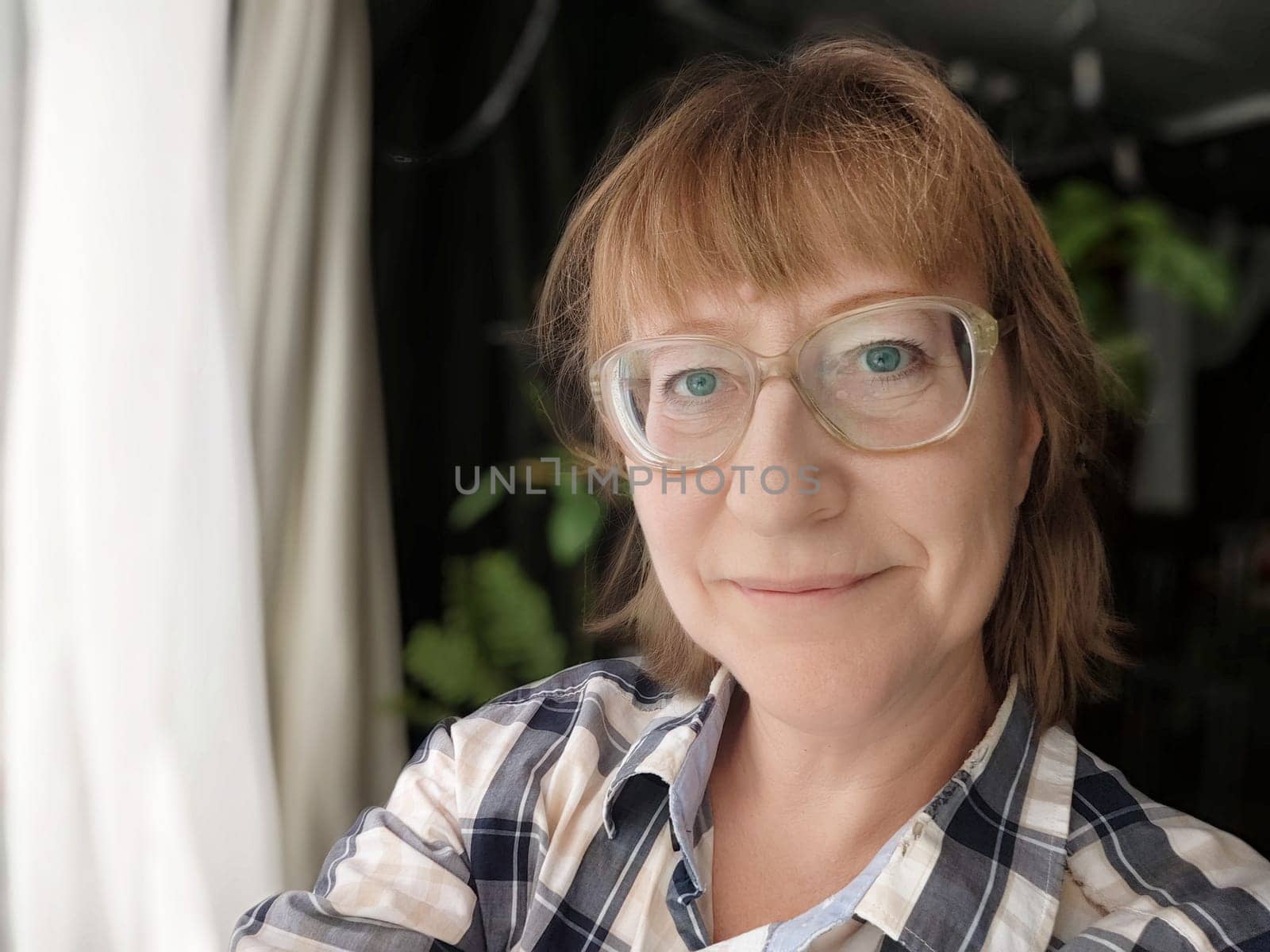 A middle-aged blonde woman captures a lively selfie during her blogging session in a warm, inviting home environment.