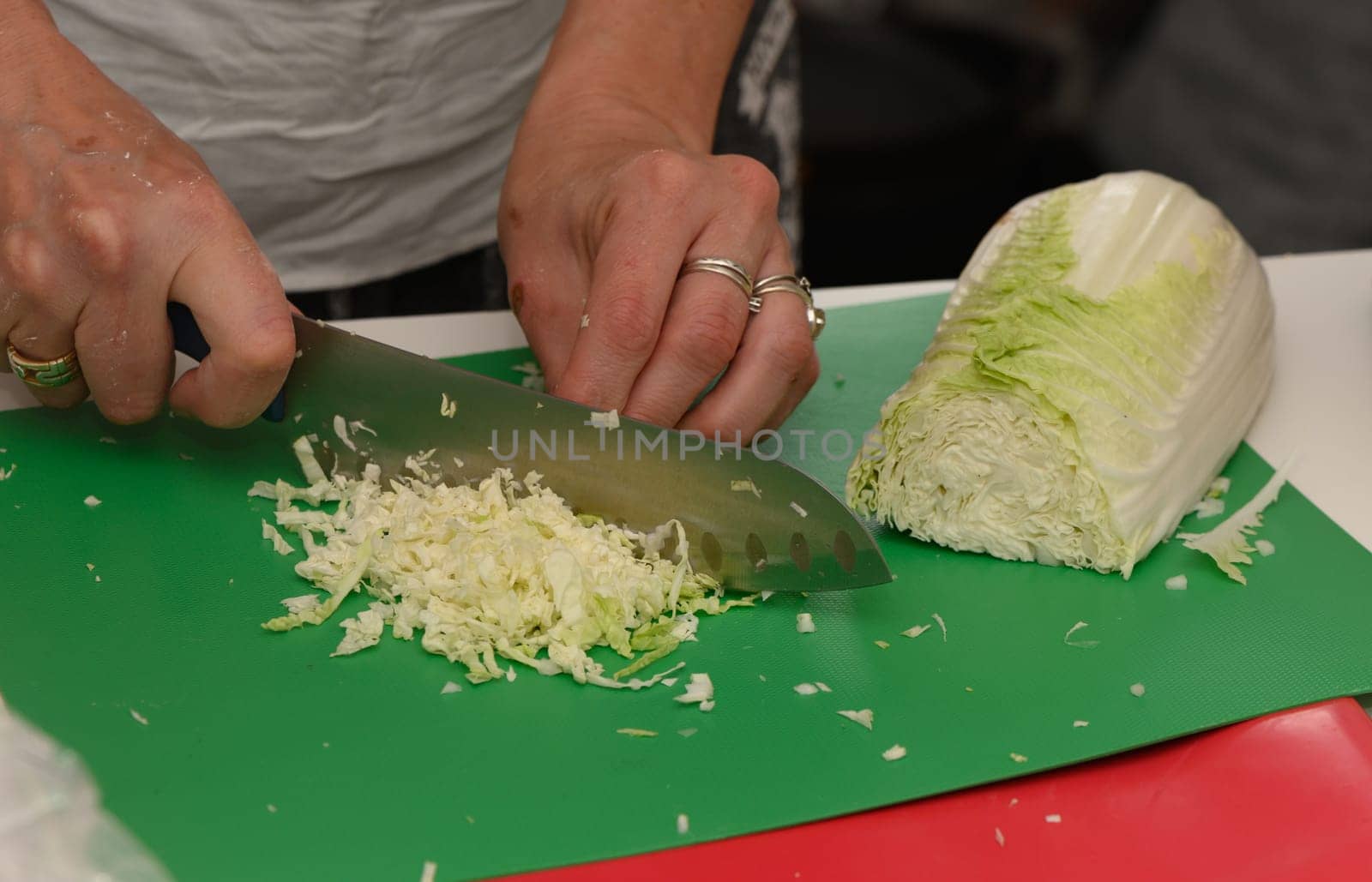 A skillful cook finely chops fresh cabbage on a green cutting board surrounded by culinary excitement and learning.
