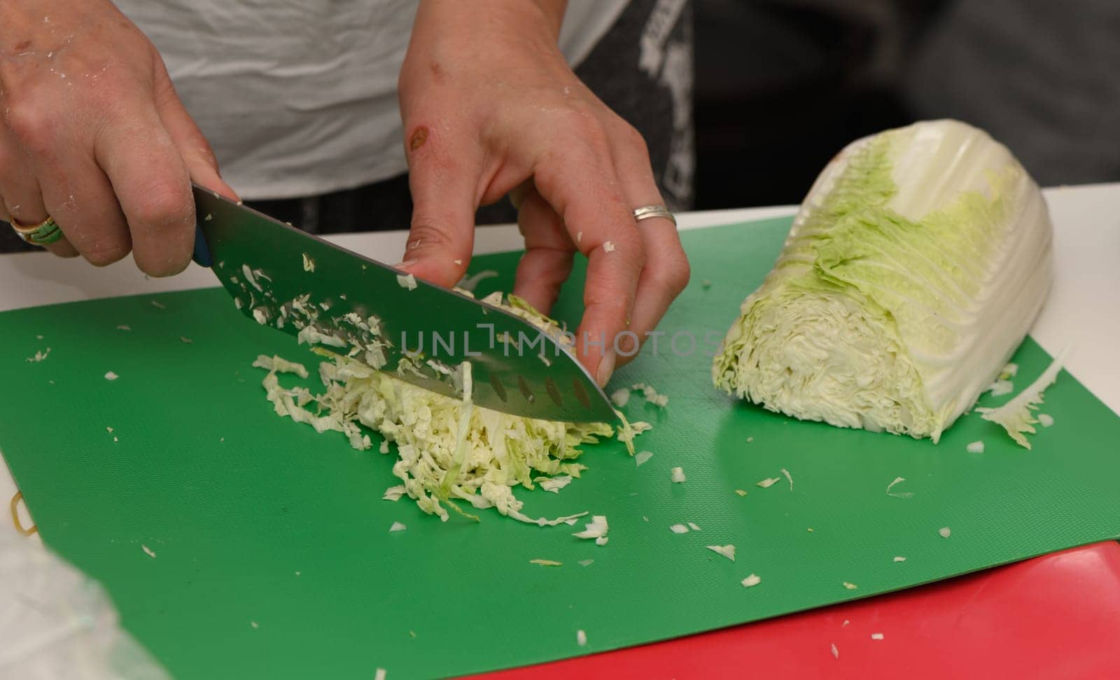 Skilled hands chop crisp cabbage on a vibrant green board, surrounded by the lively atmosphere of kitchen activity.