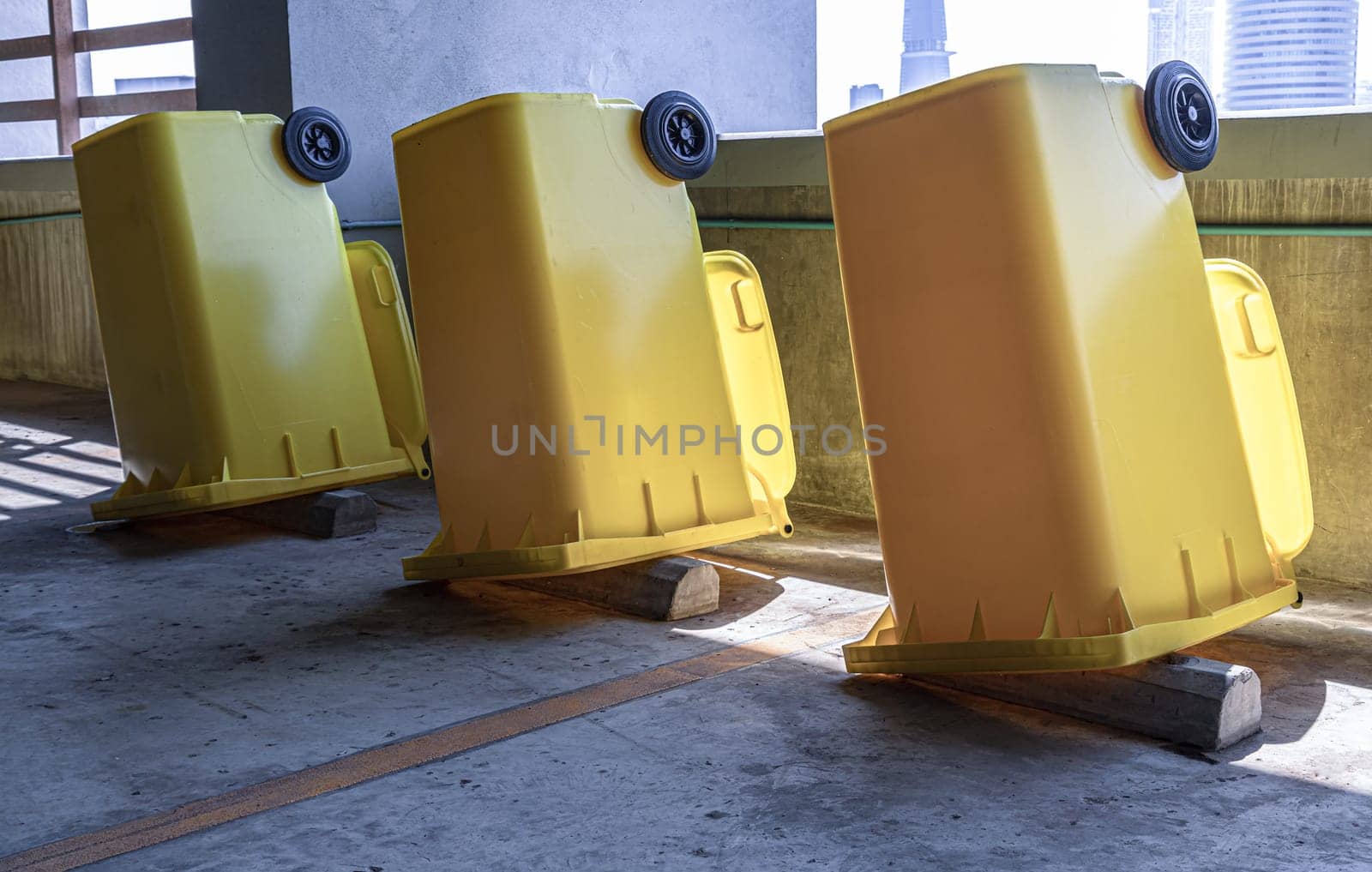 Bangkok, Thailand - Jan 18, 2025 -  Perspective view of Yellow large plastic rubbish bins and turn upside down to dry near concrete wall on parking lot of condominium building. After cleaning big plastic yellow garbages container, Plastic trash with lid for general waste, use it as your wallpaper, poster and space for text, selective focus.