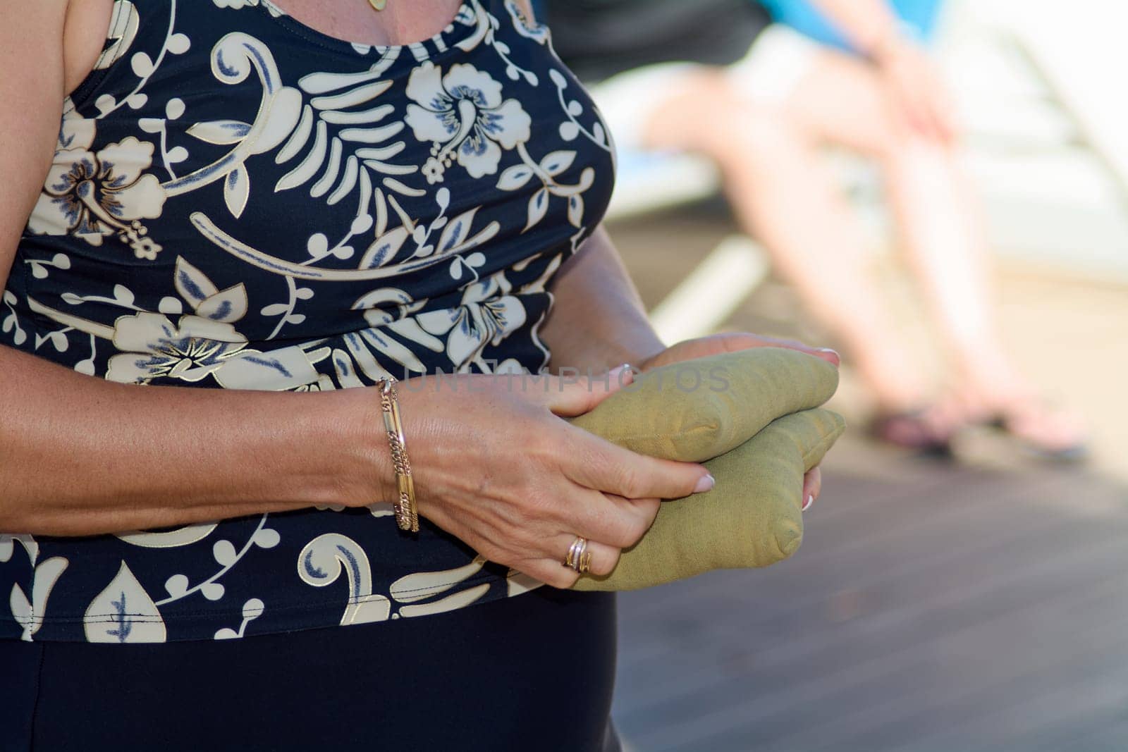 Energetic composition of hands clutching bean bags during a cornhole match, showing details like jewelry, floral design, and summer warmth.