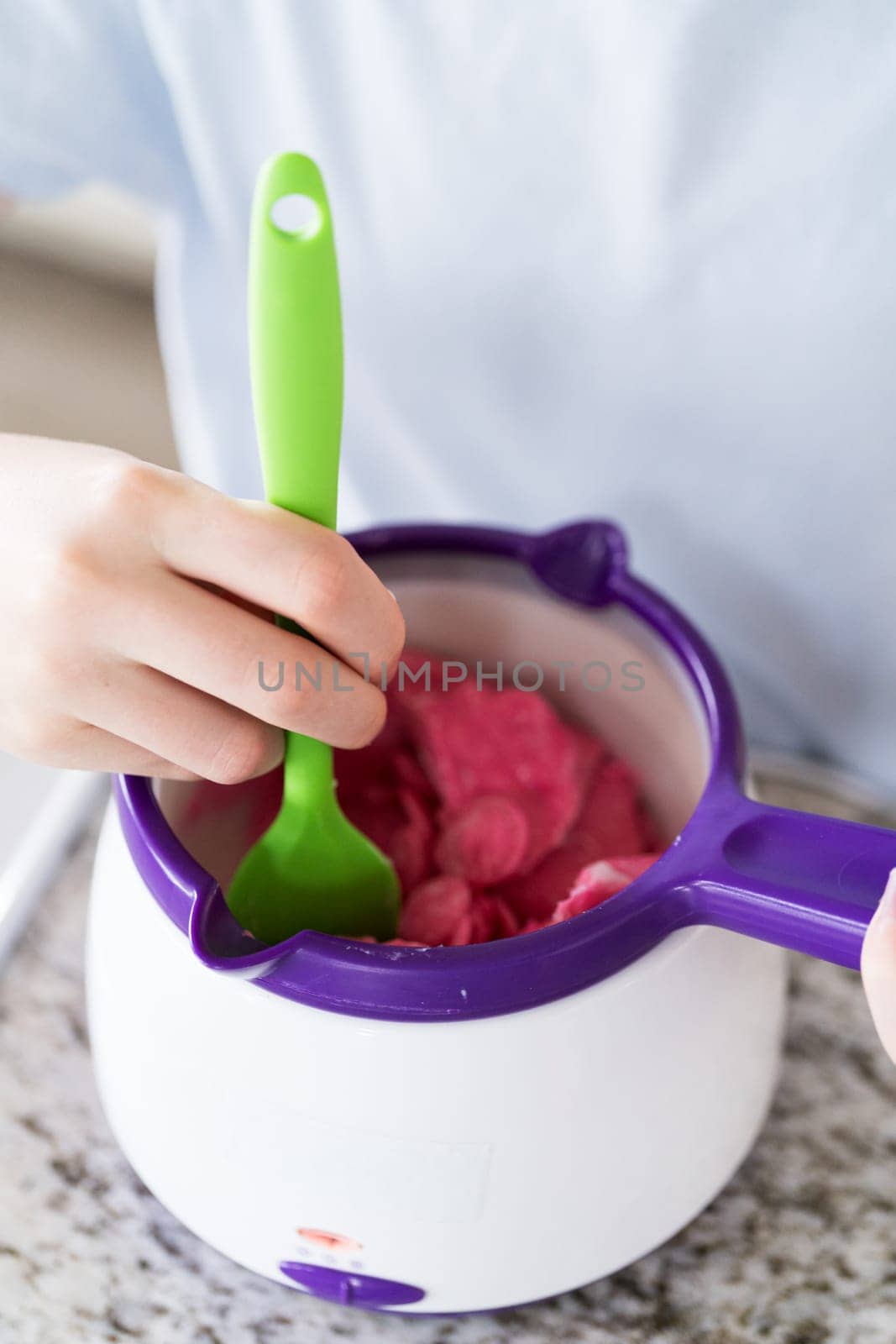 Eager eyes focus on the pot of vibrant, melting candy as a young cook gently swirls the mixture, poised to transform plain snacks into delectable treats.