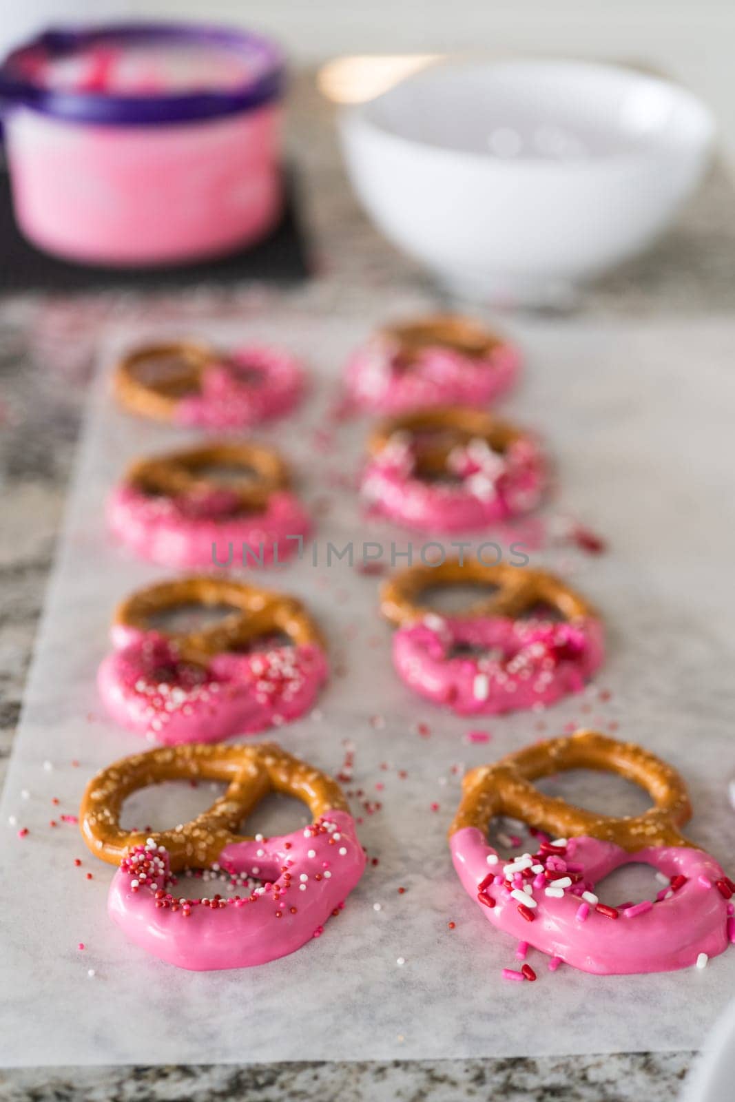 Freshly dipped and still glistening, these crunchy pretzels are lovingly adorned with pink chocolate and a scattering of colorful sprinkles, promising a feast for the senses.