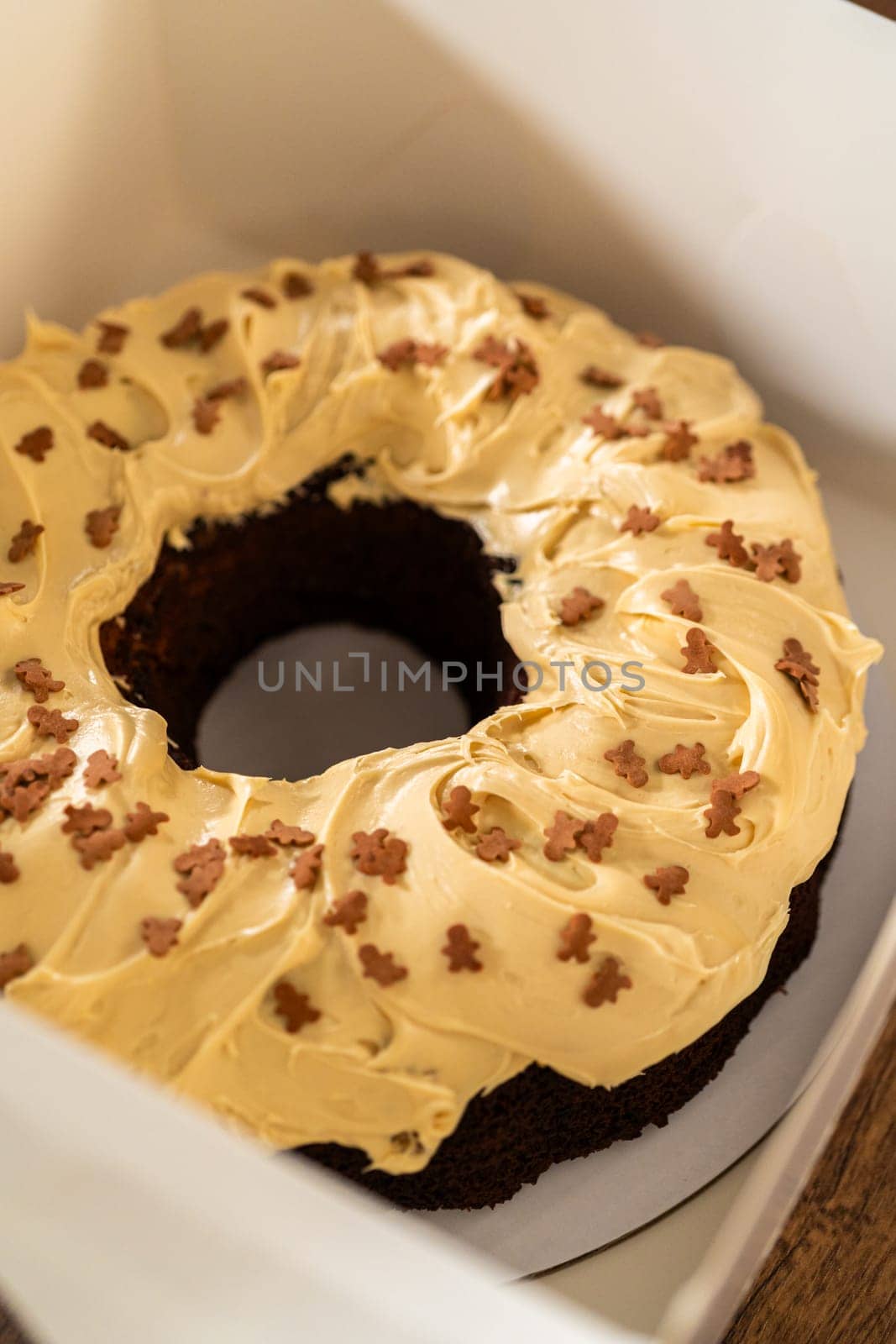 Carefully placing the gingerbread bundt cake, adorned with salted caramel frosting and gingerbread sprinkles, into a white paper bundt cake box with a clear window for gifting.