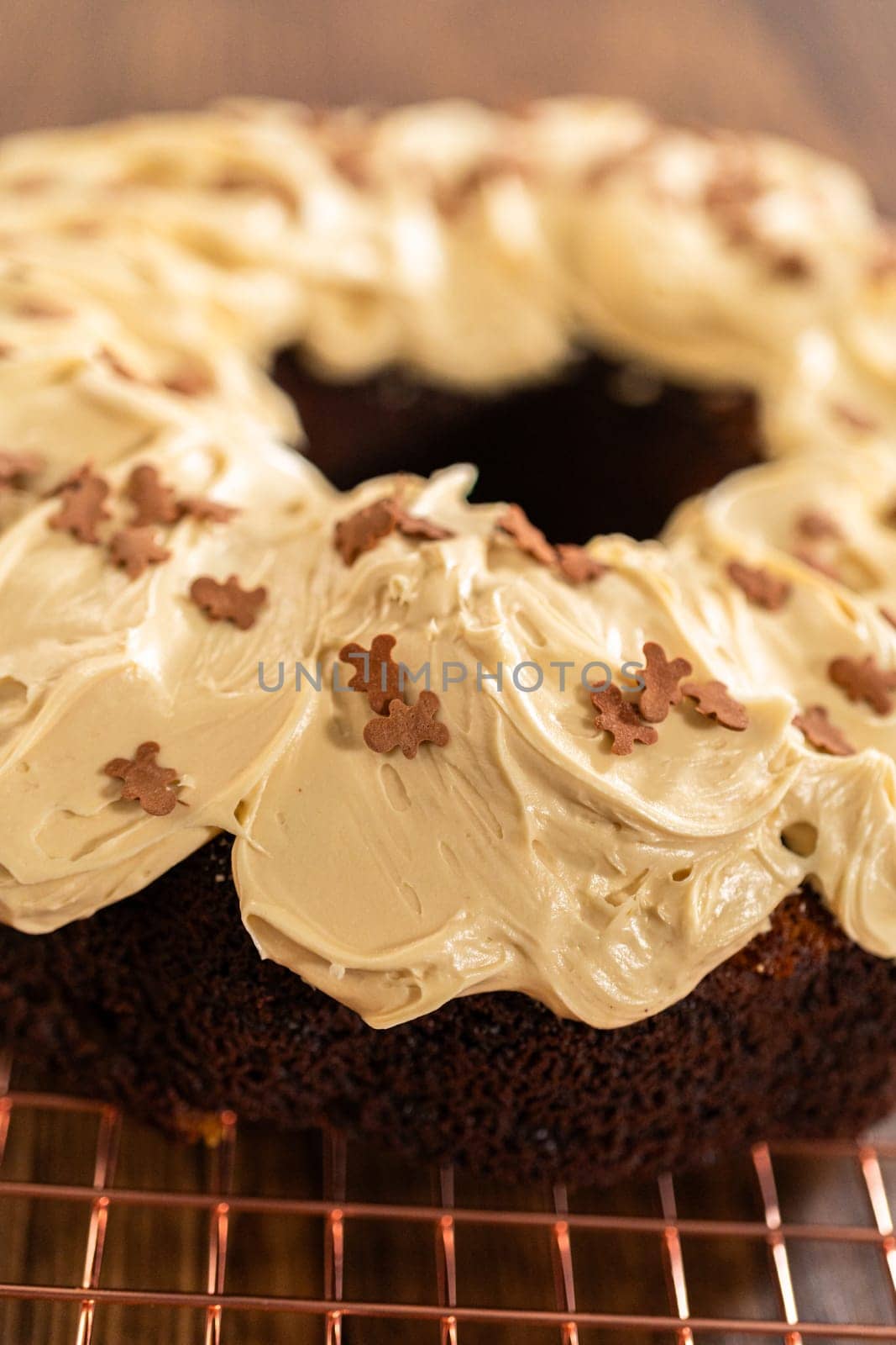 A gingerbread bundt cake being generously frosted with salted caramel frosting and topped with delightful gingerbread sprinkles.