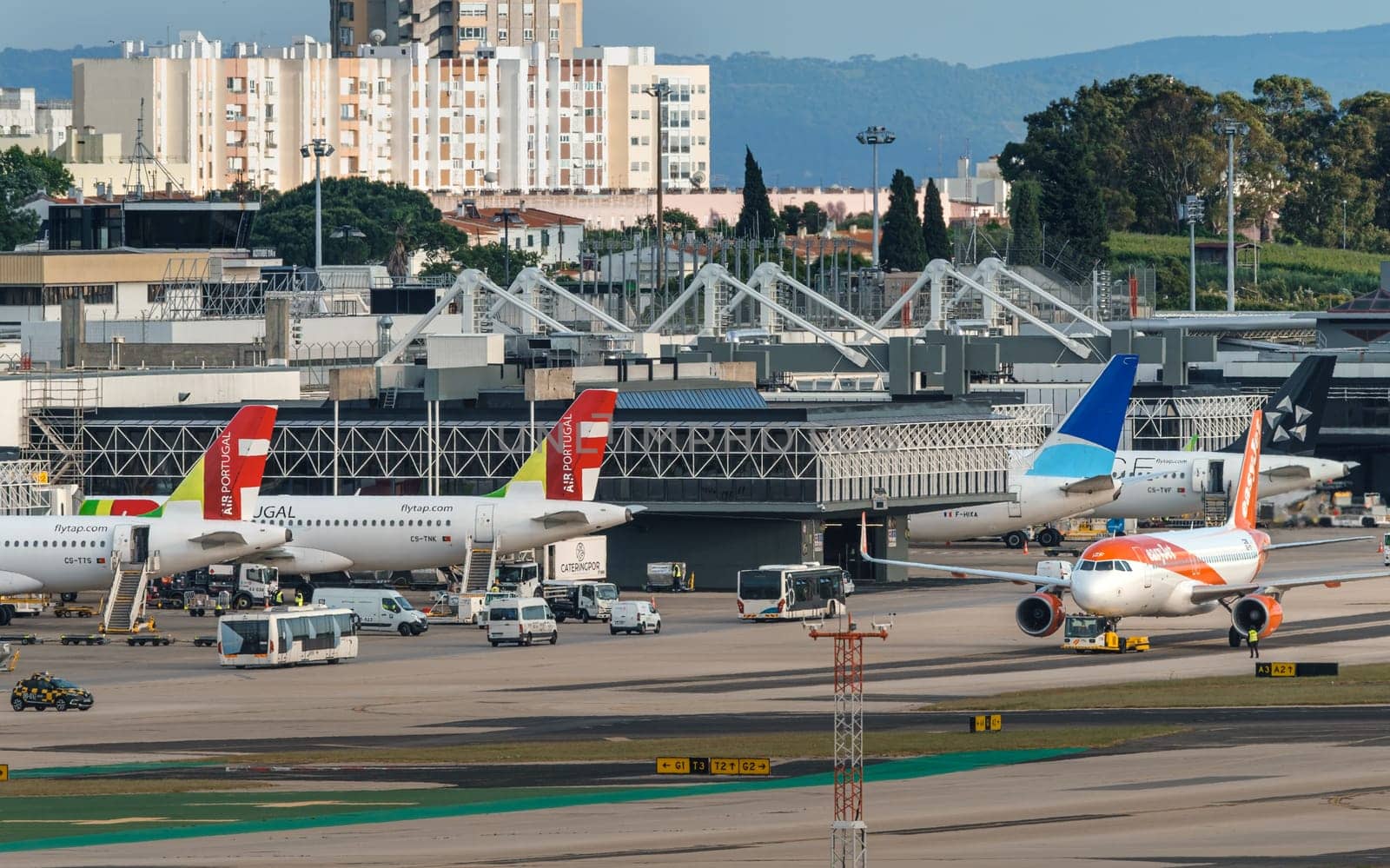 Lisbon, Portugal - Apr 24, 2024: TAP, ASL Airlines and EasyJet airplanes in Lisbon airport ready for boarding and takeoff on sunny day, clear blue sky. Ground support vehicles and airport Terminal 1 infrastructure, city buildings in background.
