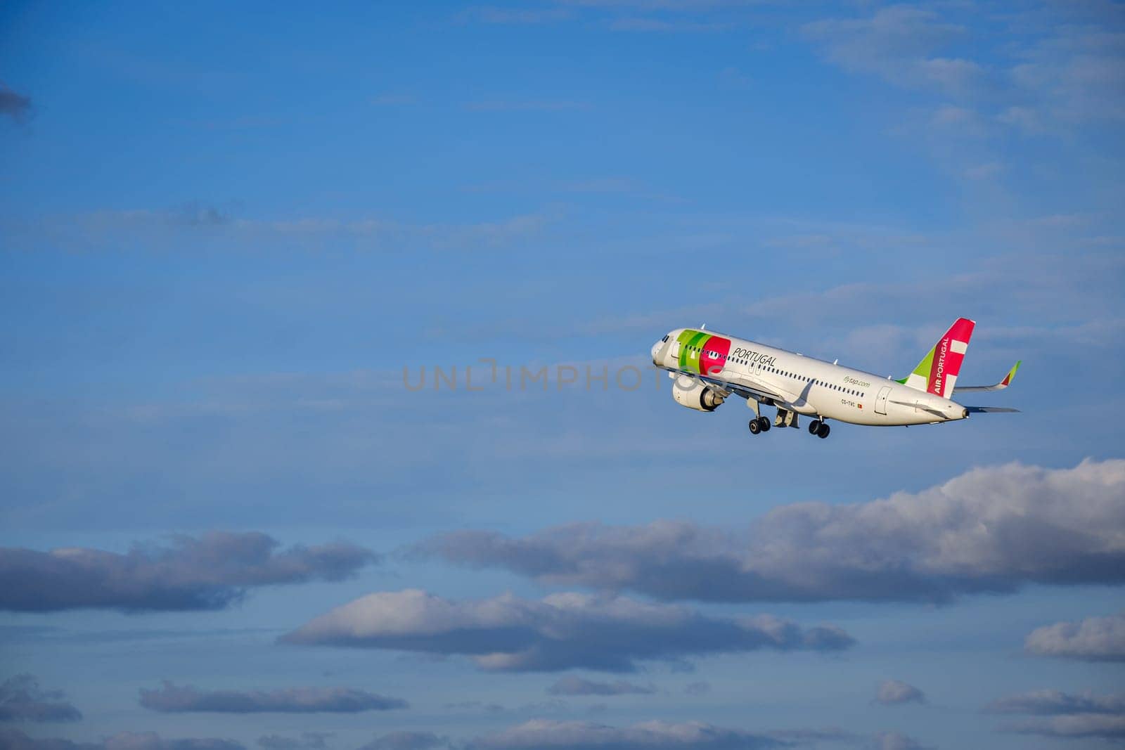 Lisbon, Portugal - Apr 29, 2024: TAP Air Portugal Airbus 320 shot mid-flight, ascending into clear blue sky with some clouds after takeoff on sunny day. Air traffic, vacations, travel, destinations, aircraft, international aviation, commercial airlines