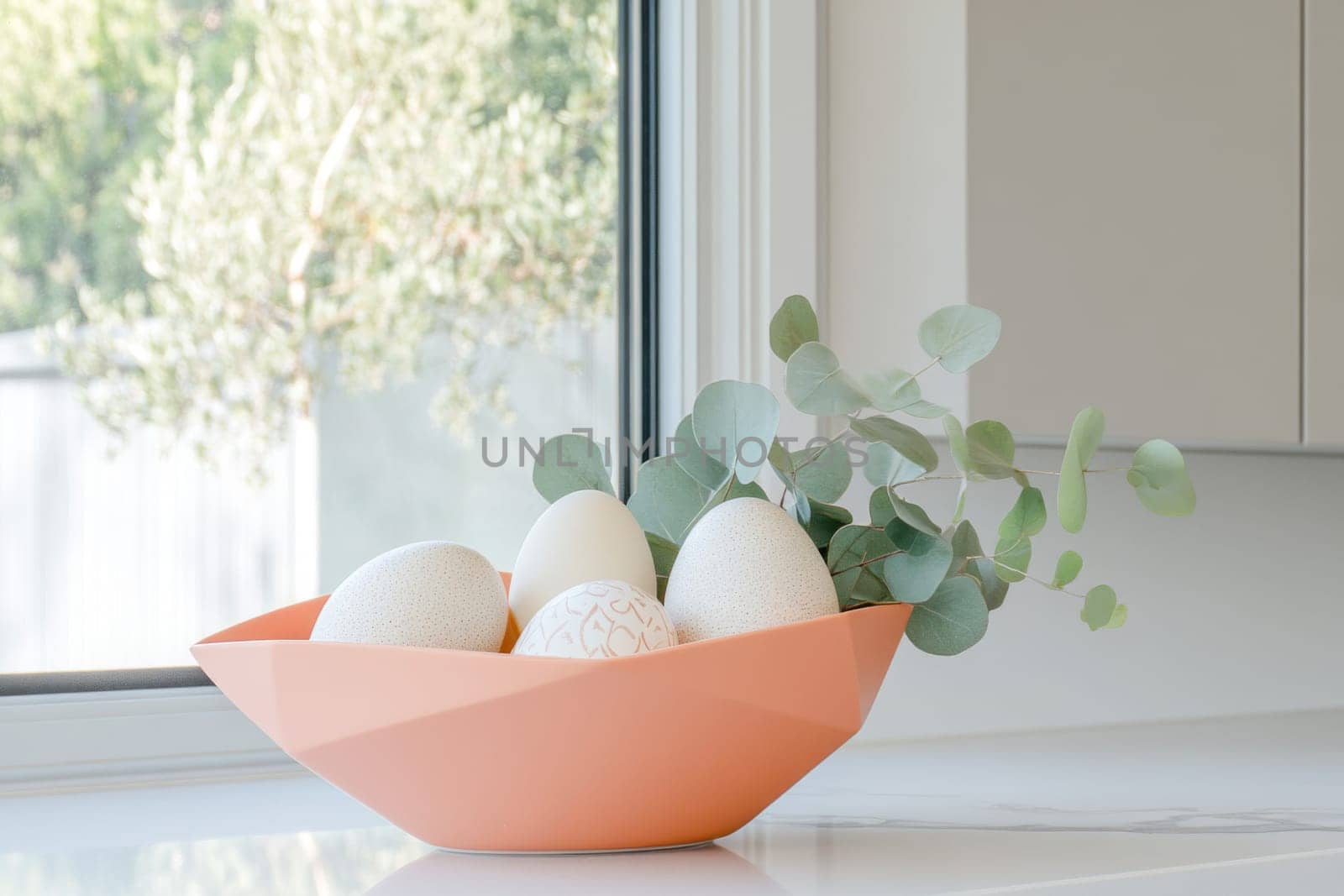 Simple colored Easter eggs arranged in a modern vessel with eucalyptus leaves make a stylish minimalist Easter centerpiece on a marble countertop, enhancing the spring ambiance.