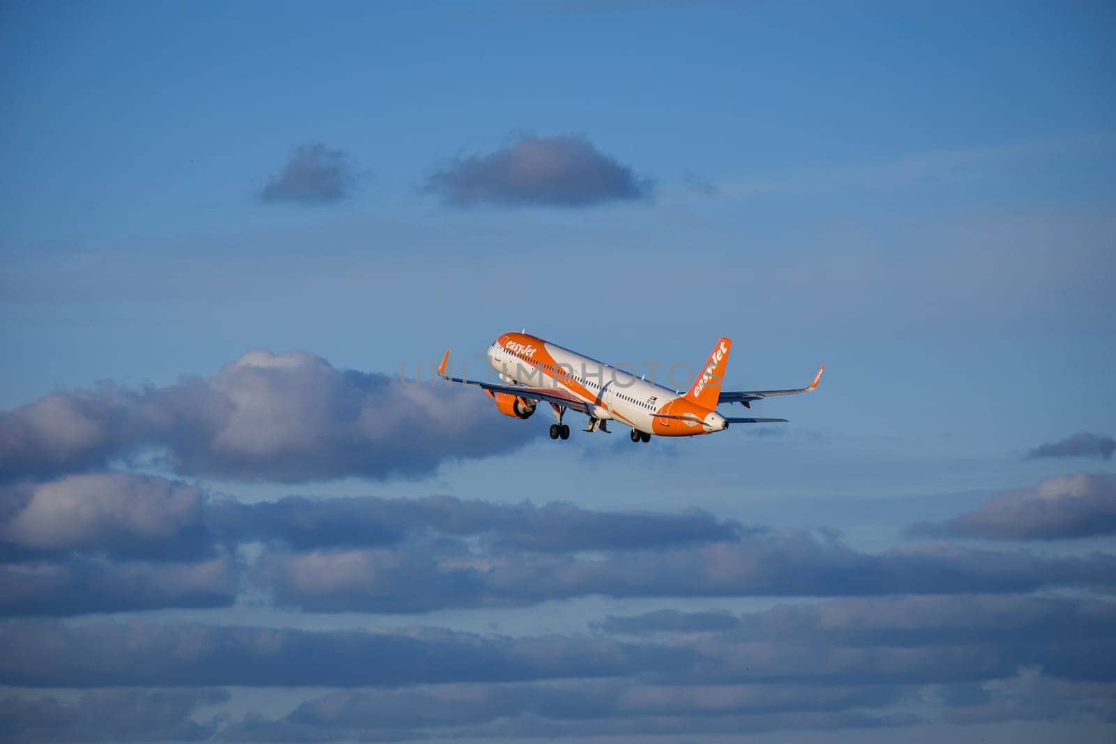 Lisbon, Portugal - Apr 29, 2024: EasyJet Airbus 321 neo aircraft shot mid-flight, ascending into clear blue sky with some clouds after takeoff on sunny day. Air traffic, vacations, travel, destinations, aircraft, low-cost airline, commercial flight