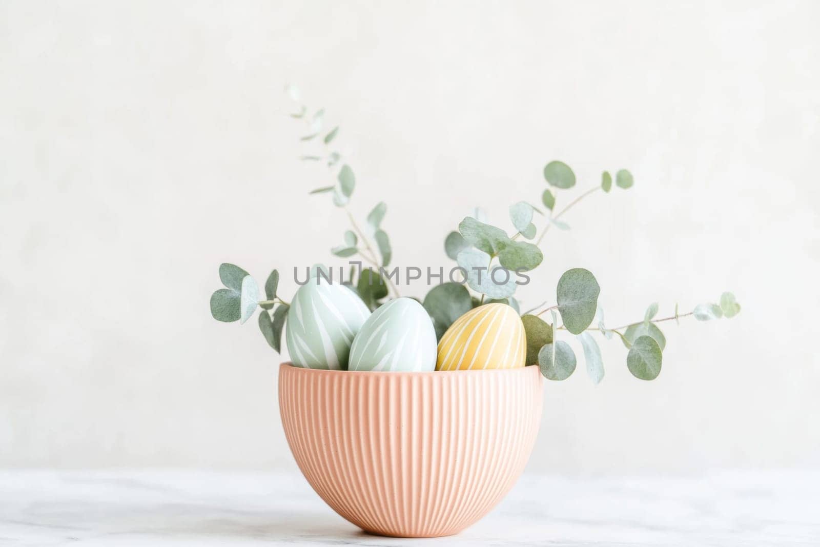 Delicate eucalyptus leaves surround primitive patterned pysanka Easter eggs in a soft textured bowl, creating a minimalist Easter centerpiece on a marble countertop, perfect for seasonal decor.