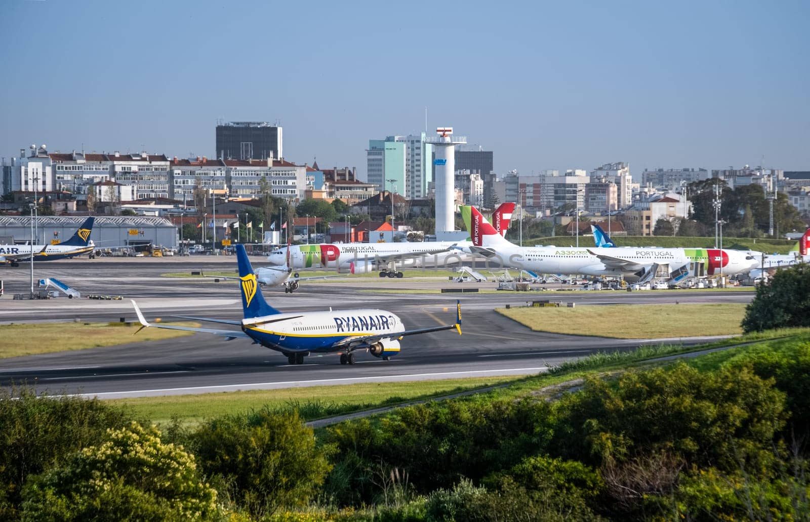Lisbon, Portugal - Apr 3, 2024: Air Portugal or TAP, Ryanair and Azores airlines airplanes parked at Lisbon airport apron, Ryanair aircraft fast moving on runway. Clear blue sky, sunny day, vacation, travel destination, city landscape in background