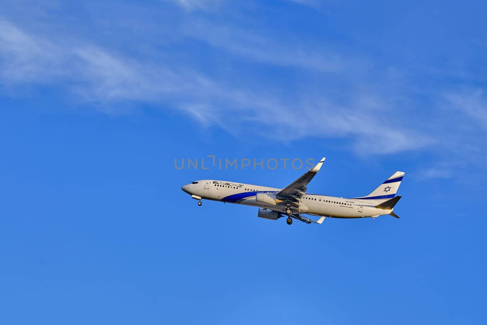 Lisbon, Portugal - Jan 14, 2025: El Al Airlines Boeing 737 shot mid-flight with landing gear extended, ready for landing on sunny day with clear blue sky and some soft clouds. Classic livery of Israel flag carrier.