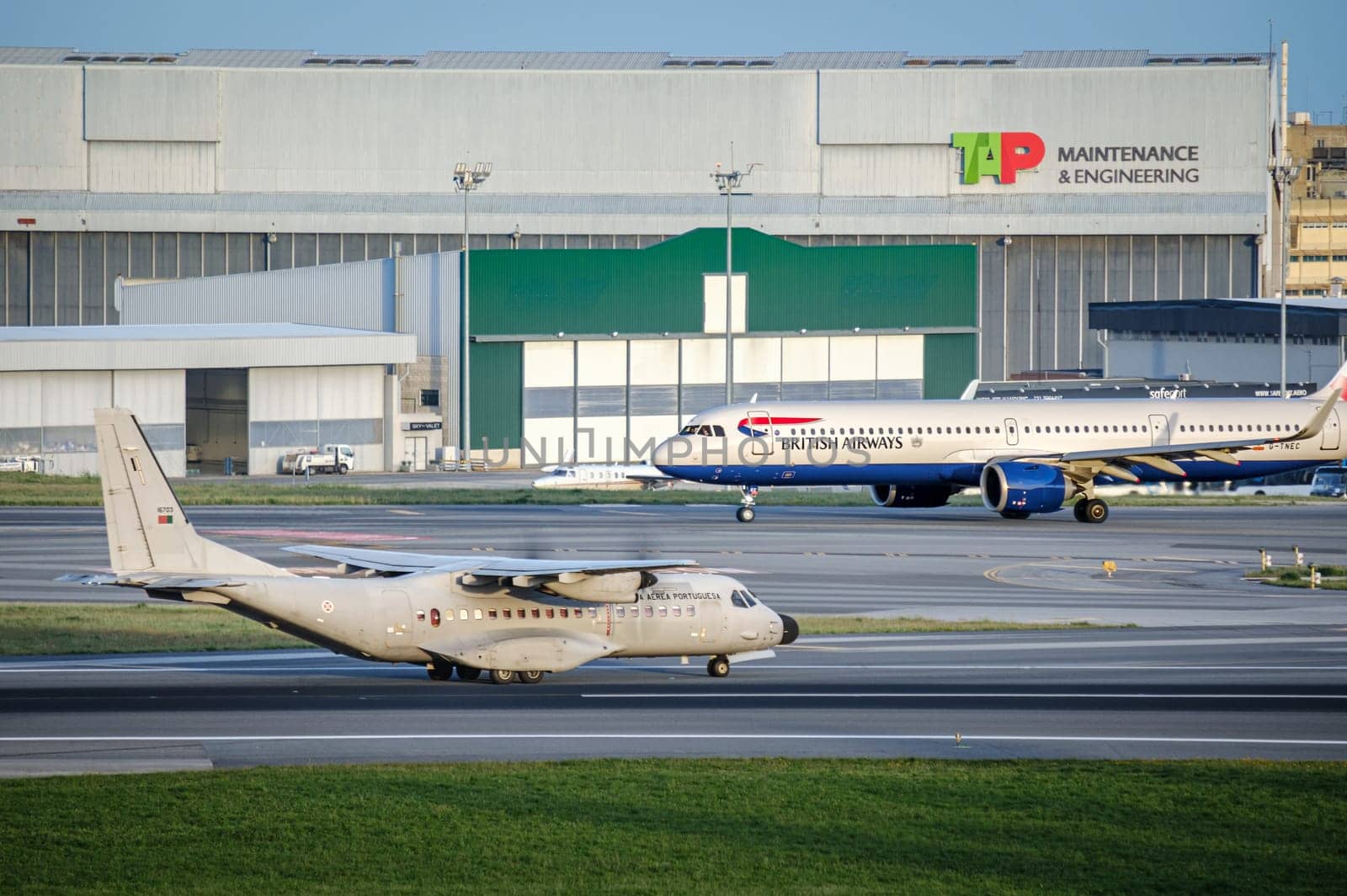 Lisbon, Portugal - Apr 3, 2024: Portuguese Air Force military transport aircraft Airbus C295 and British Airways Airbus A321neo airplane taxiing at Lisbon Airport. TAP Maintenance and Engineering hangar and infrastructure, busy international hub