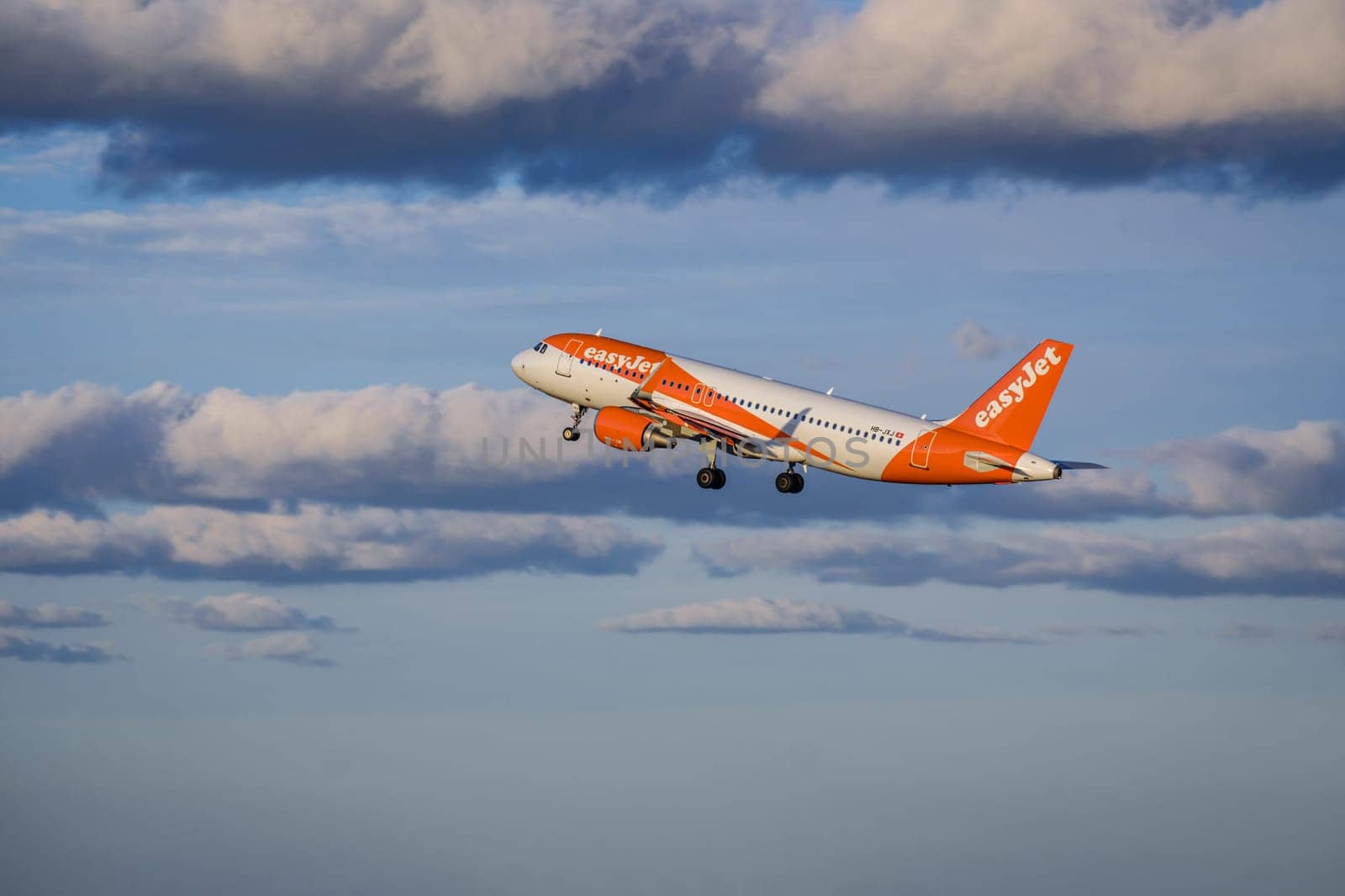 Lisbon, Portugal - Apr 29, 2024: EasyJet Airbus 320 aircraft shot mid-flight, ascending into clear blue sky with some clouds after takeoff on sunny day. Air traffic, vacations, travel, destinations, aircraft, low-cost airline, commercial flight
