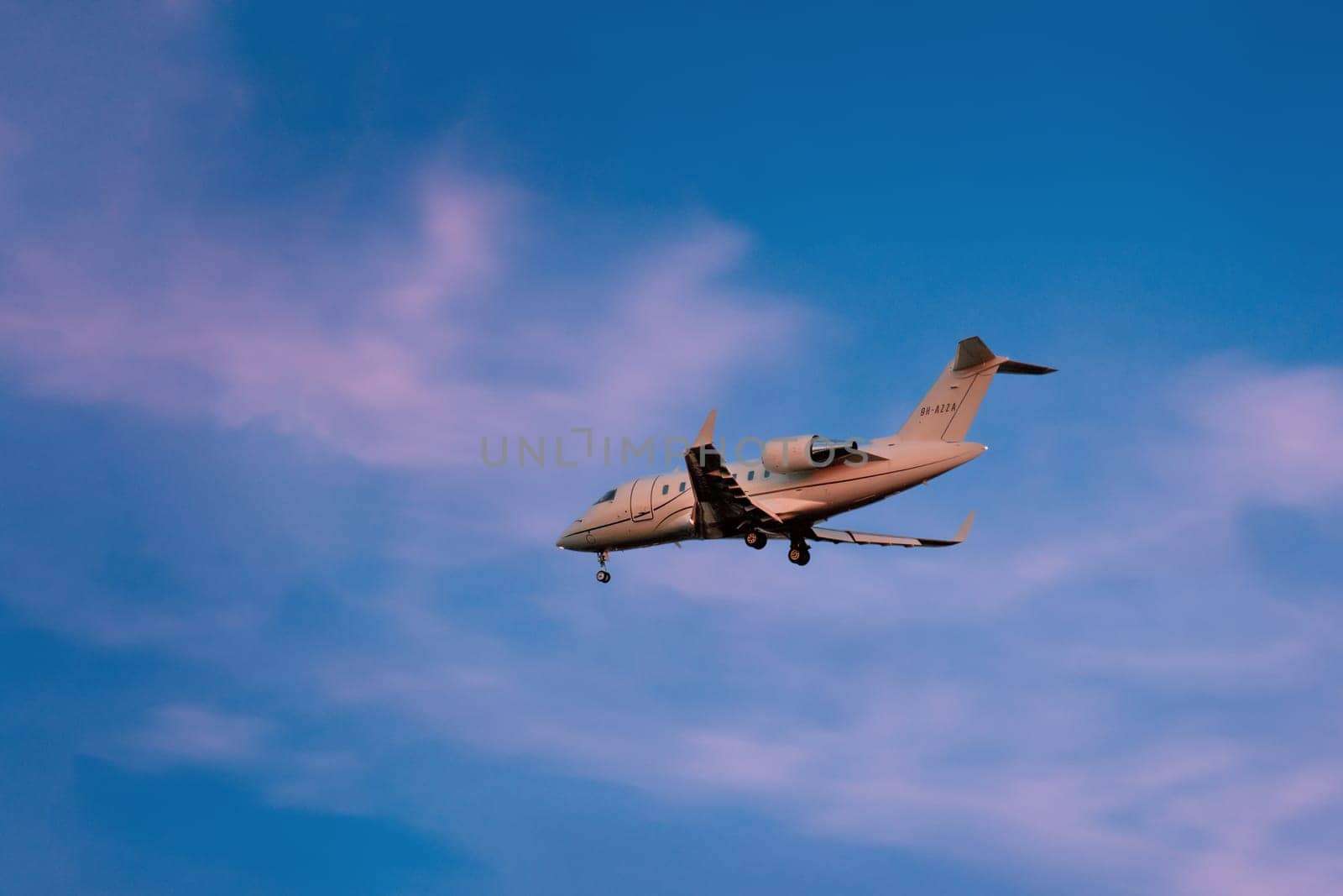 Lisbon, Portugal - Jan 14, 2025: Bombardier Challenger 300 private jet shot mid-descent with landing gear extended. Aircraft flying in colorful sunset sky with some clouds, luxury aviation, executive travel, private travel comfort.