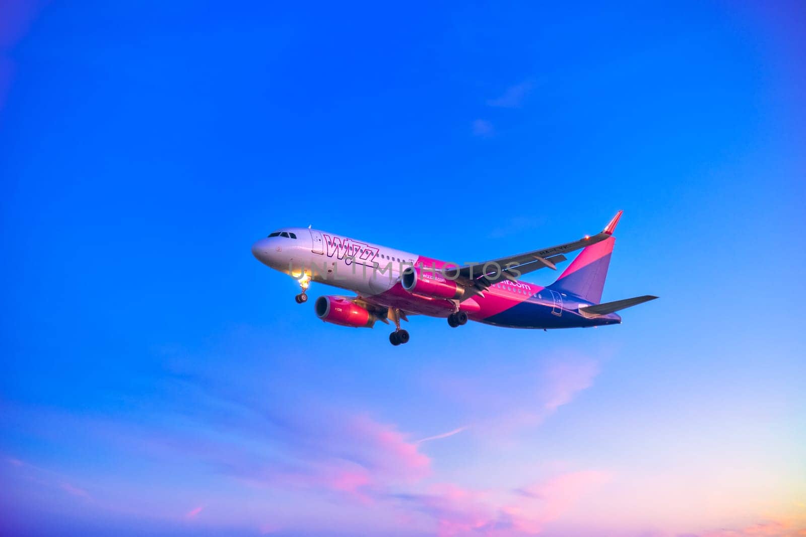 Lisbon, Portugal - Jan 14, 2025: Wizz Air Airbus A320 aircraft shot mid-descent with landing gear extended, flying in colorful sunset sky. Low-cost airline, budget-friendly European air travel, weekend getaway, holiday, vacation.