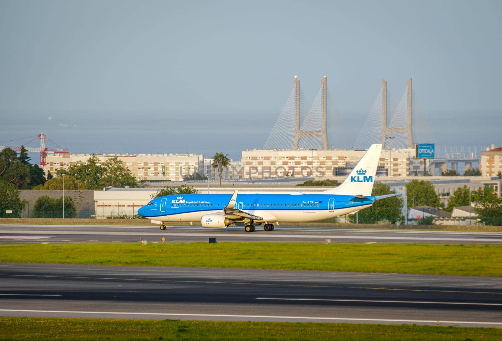 Lisbon, Portugal - Apr 3, 2024: KLM Royal Dutch Airlines aircraft Cityhopper Embraer E190 taxiing on runway at Lisbon airport on sunny day, clear sky and Vasco da Gama bridge in background. Vacations, weekend getaway, summer travel destination