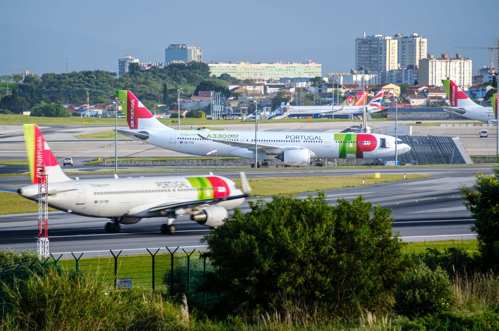 Lisbon, Portugal - Apr 3, 2024: Air Portugal or TAP airplanes parked at Lisbon airport apron, TAP aircraft fast moving on runway. Clear blue sky, sunny day, summer, vacation, travel destination, city landscape in background. British airways, EasyJet