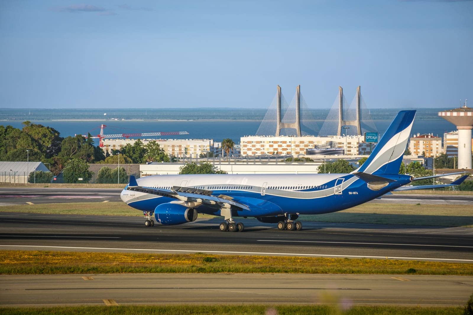 Lisbon, Portugal - Apr 3, 2024: HiFly Malta Airline Airbus 330-300 airplane taxiing on runway at Lisbon airport on sunny day, clear sky and bridge in background. Vacations, weekend getaway, summer travel destination, river, aircraft takeoff, landing