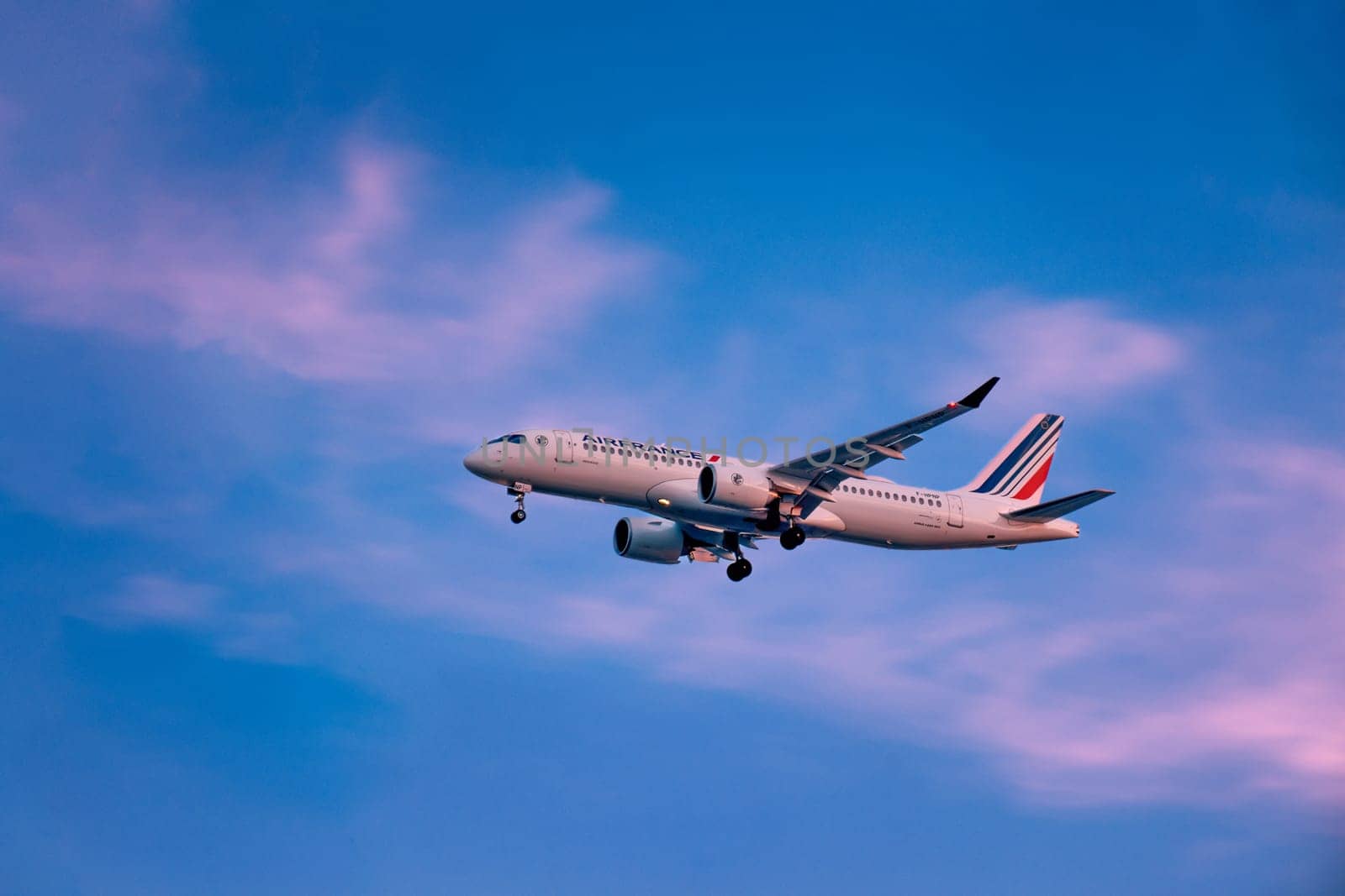 Lisbon, Portugal - Jan 14, 2025: Air France Airbus A220 aircraft shot mid-descent with landing gear extended, flying in beautiful sunset sky with colorful clouds. Flag carrier of France, international flight, airplane livery, business and holiday
