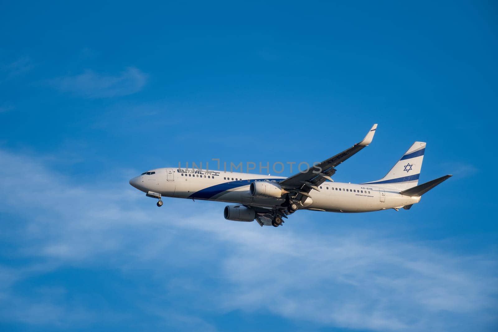 Lisbon, Portugal - Jan 14, 2025: El Al Airlines Boeing 737 shot mid-flight with landing gear extended, ready for landing on sunny day with clear blue sky and some soft clouds. Classic livery of Israel flag carrier.