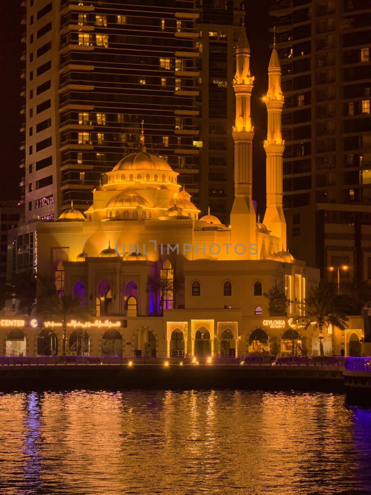 UAE, Dubai, 10 December 2024: Mosque of Muhammad Ibn Ahmad Al-Mullah against the backdrop of skyscrapers at night in Dubai Marina, yachts sailing by, reflection of night lighting on the water. High quality photo
