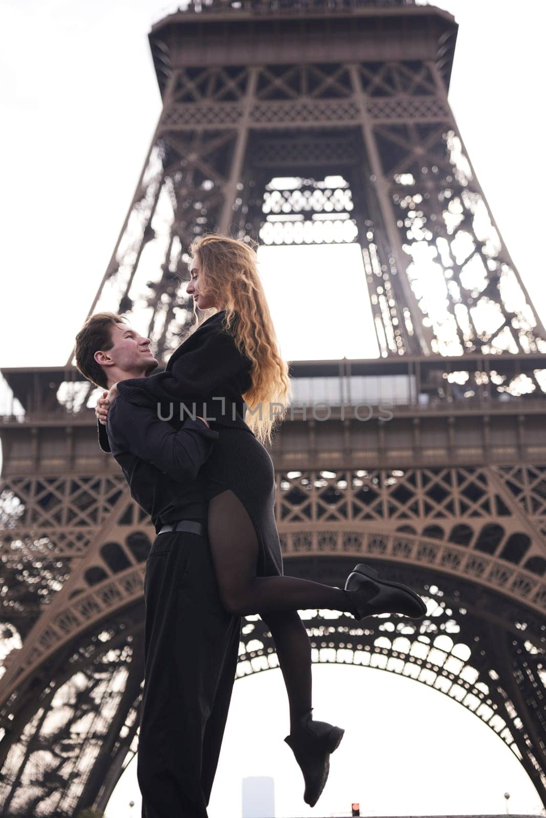A romantic couple shares an intimate moment in Paris. The man lifts the woman in a loving embrace beneath the Eiffel Tower, symbolizing passion, connection, and the magic of love.