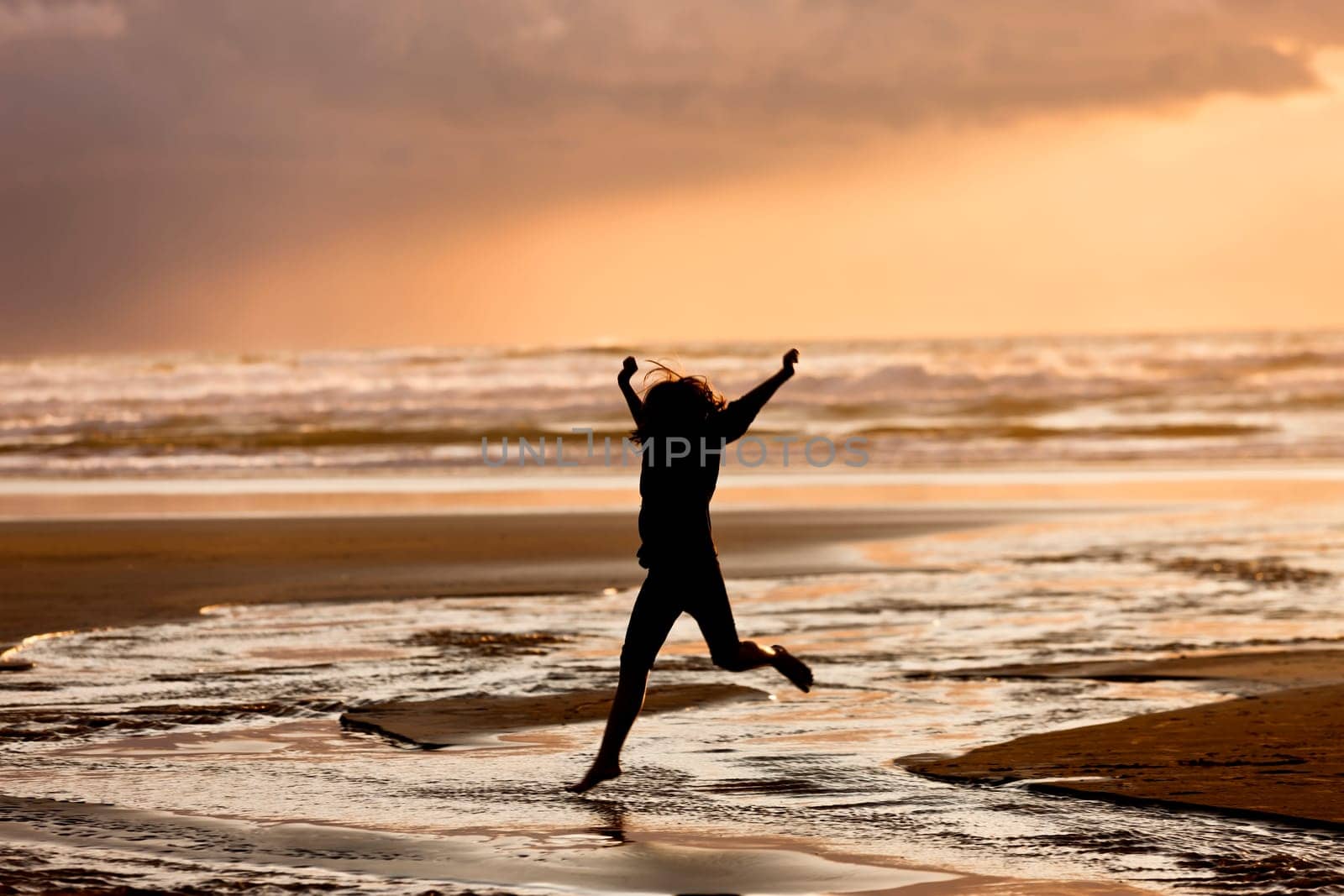 A girl in silhouette at sunset leaps into the creek on Nye Beach that flows into the ocean in Newport, Oregon.