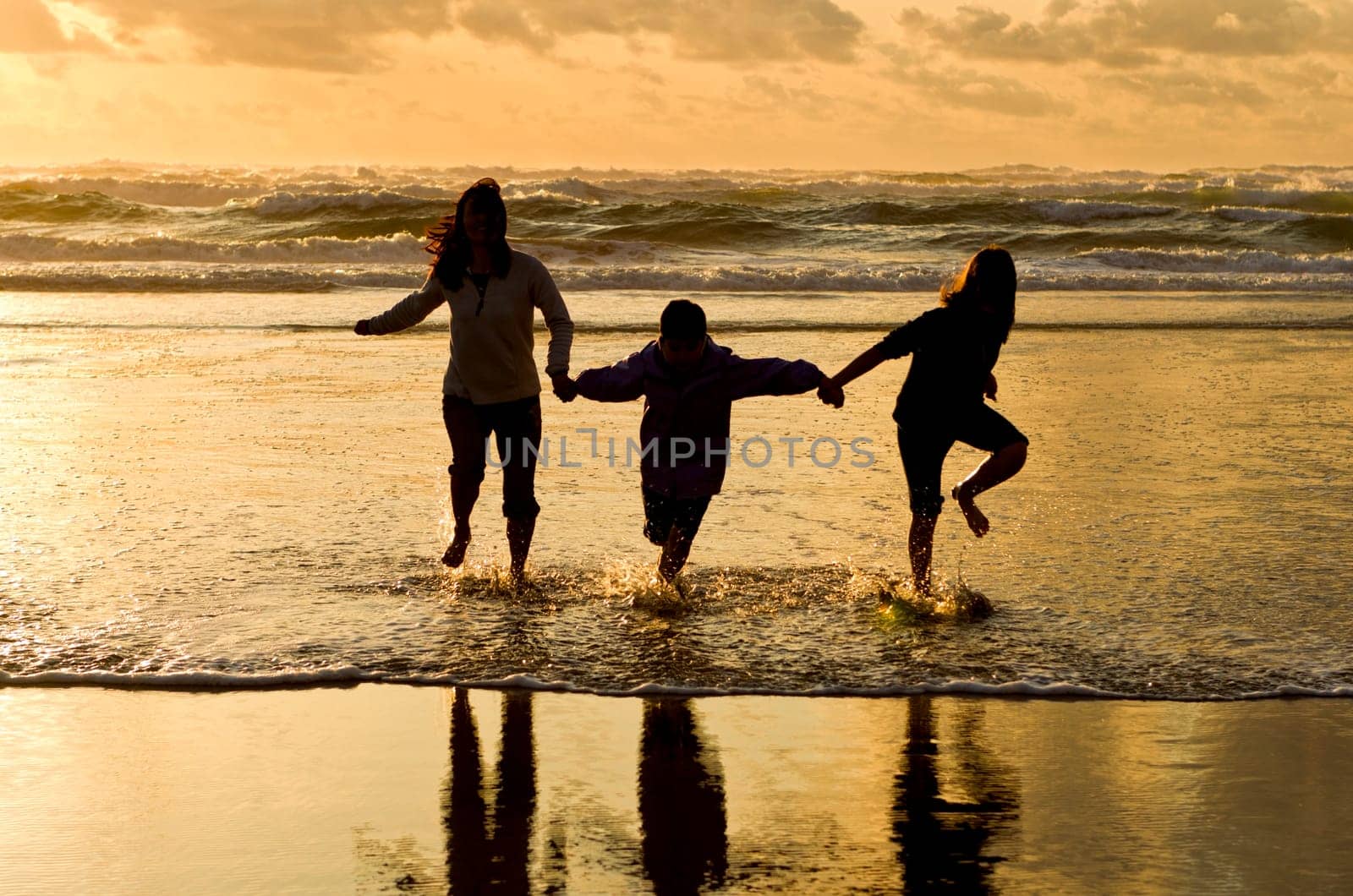 A mother, daughter, and son, walk in the water at the beach in Newport, Oregon.