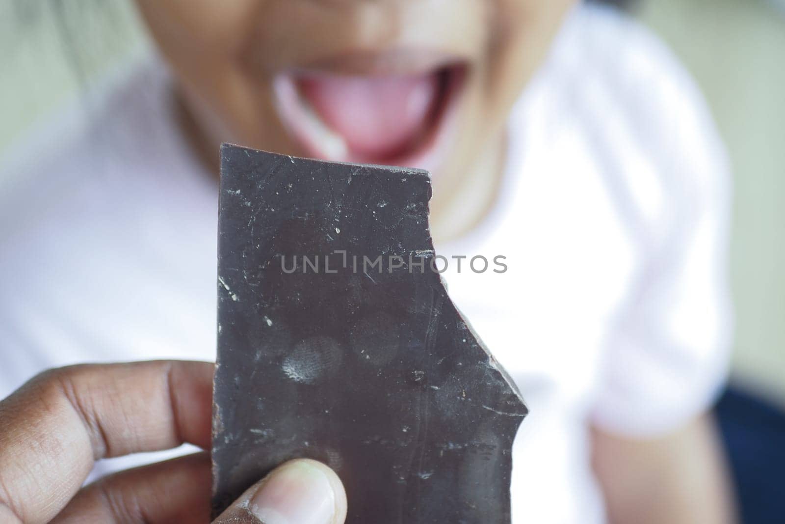 Child joyfully prepares to eat a large piece of chocolate candy while smiling.