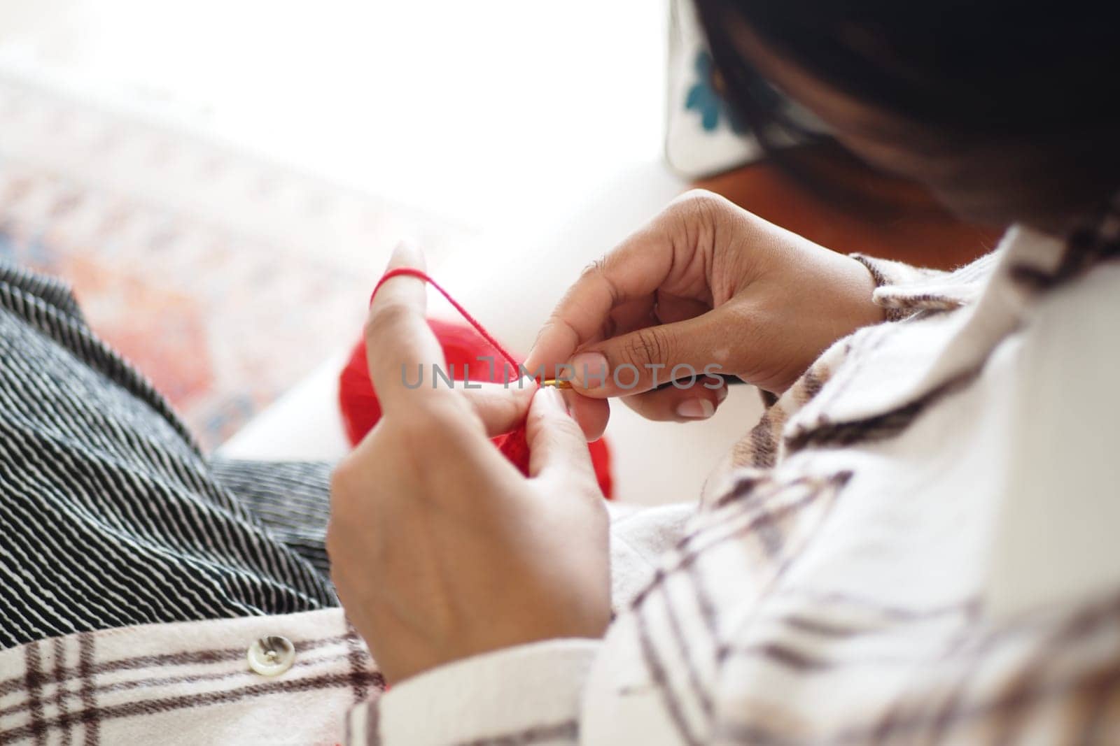 A person carefully sews a button onto a piece of clothing using thread.