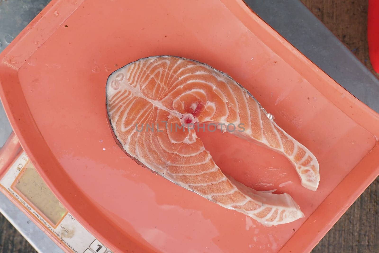 A salmon fillet is carefully placed on a scale at a market.
