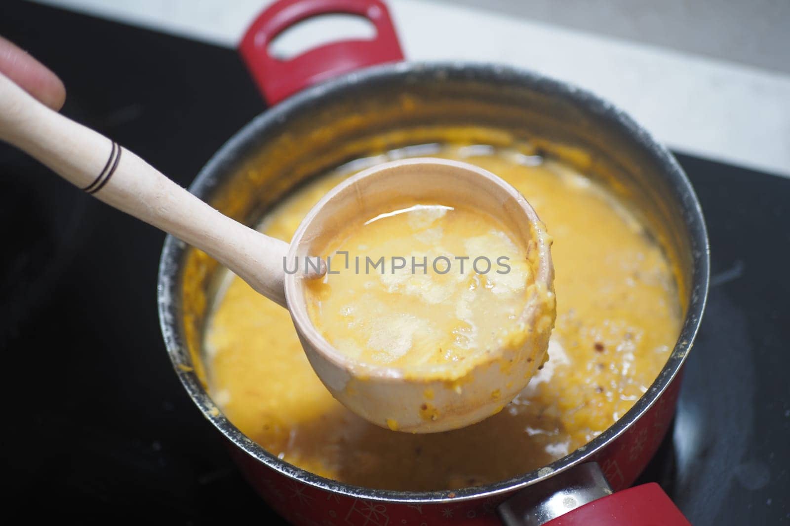 A wooden ladle scoops soup from a red pot on the stovetop.