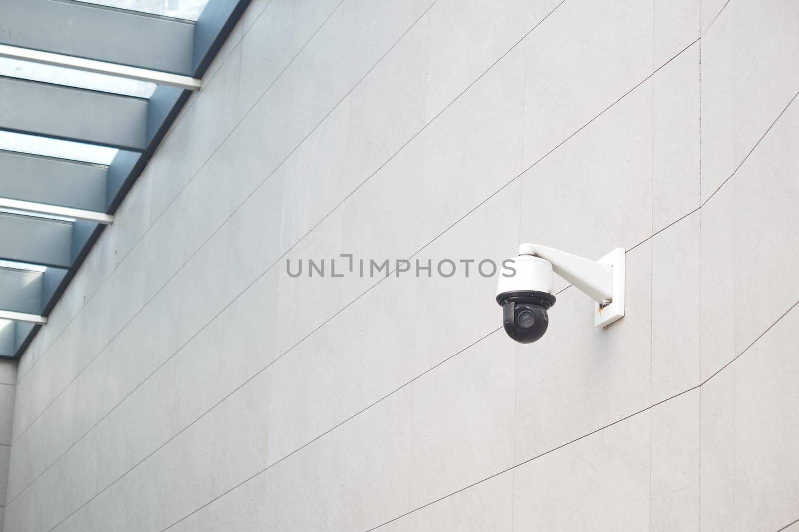 A security camera is installed on a smooth wall below a glass ceiling.