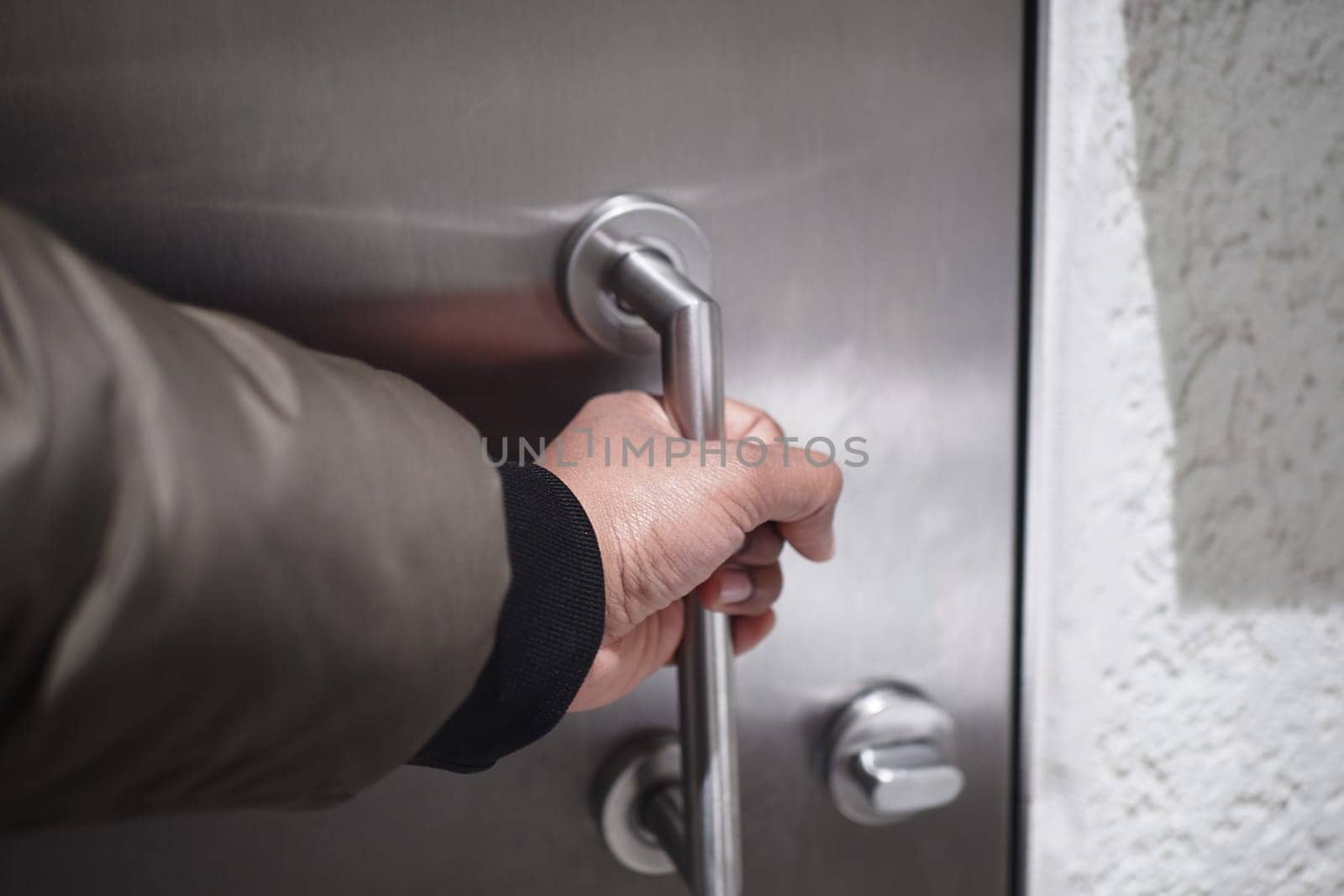 A person reaches for a sleek metallic door handle with intent.