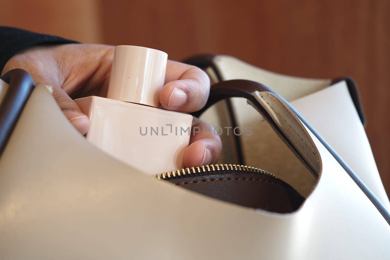 A hand is gently inserting a perfume bottle into a handbag.