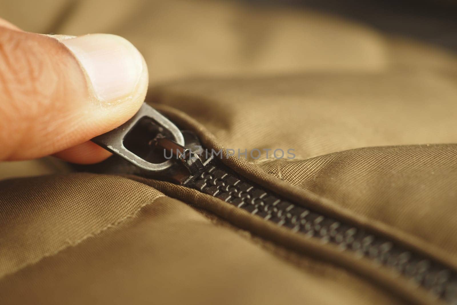 Close-up of a hand gripping a zipper on a brown jacket during daytime.