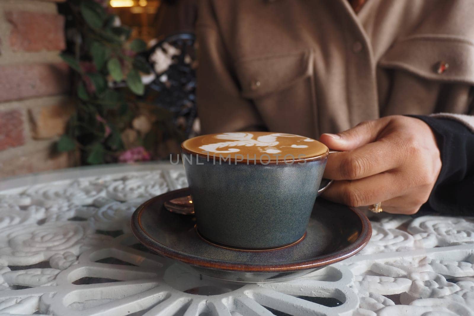 A person enjoys a beautifully crafted coffee at a cafe table.