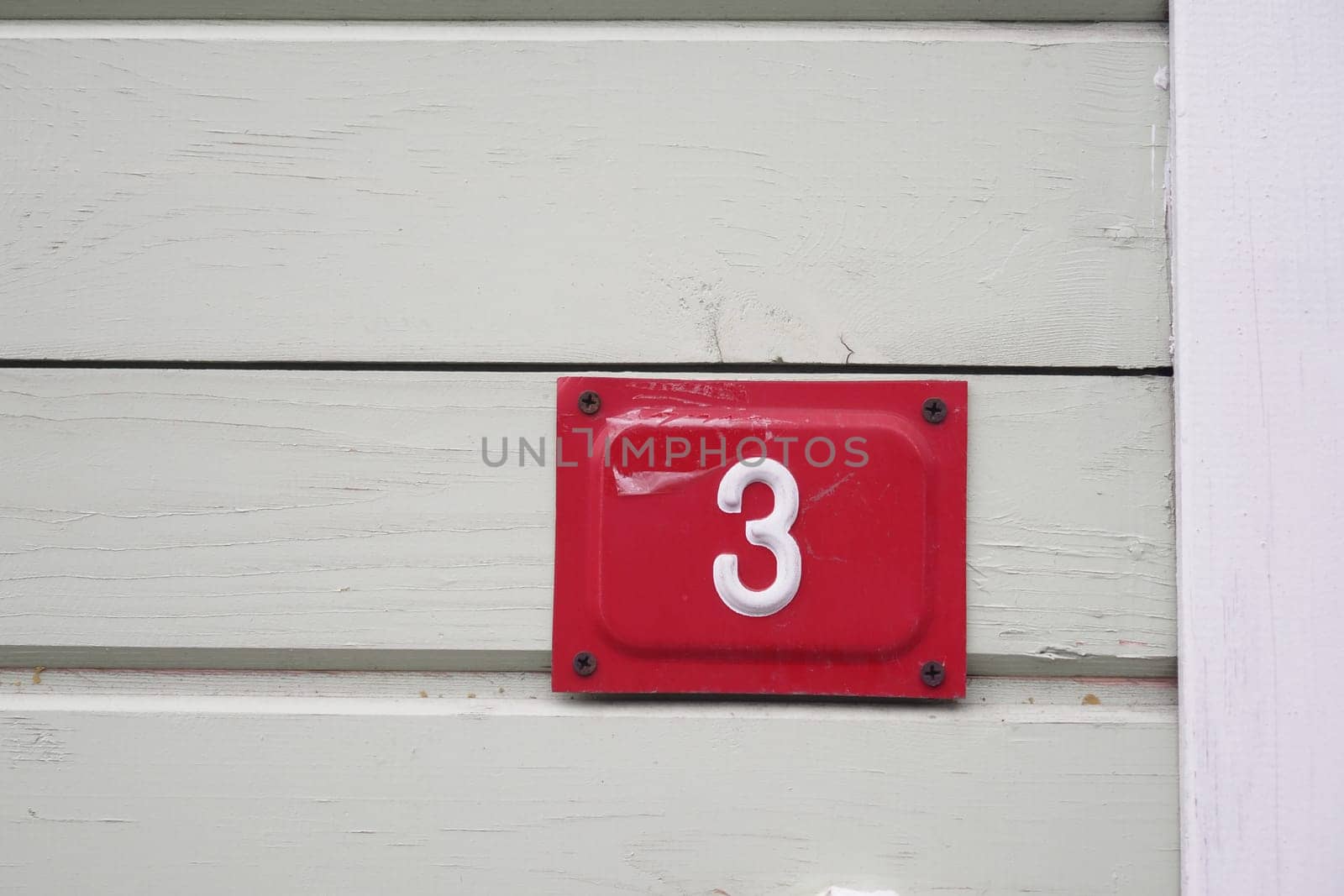 A bright red number three is mounted on a light green wooden wall.