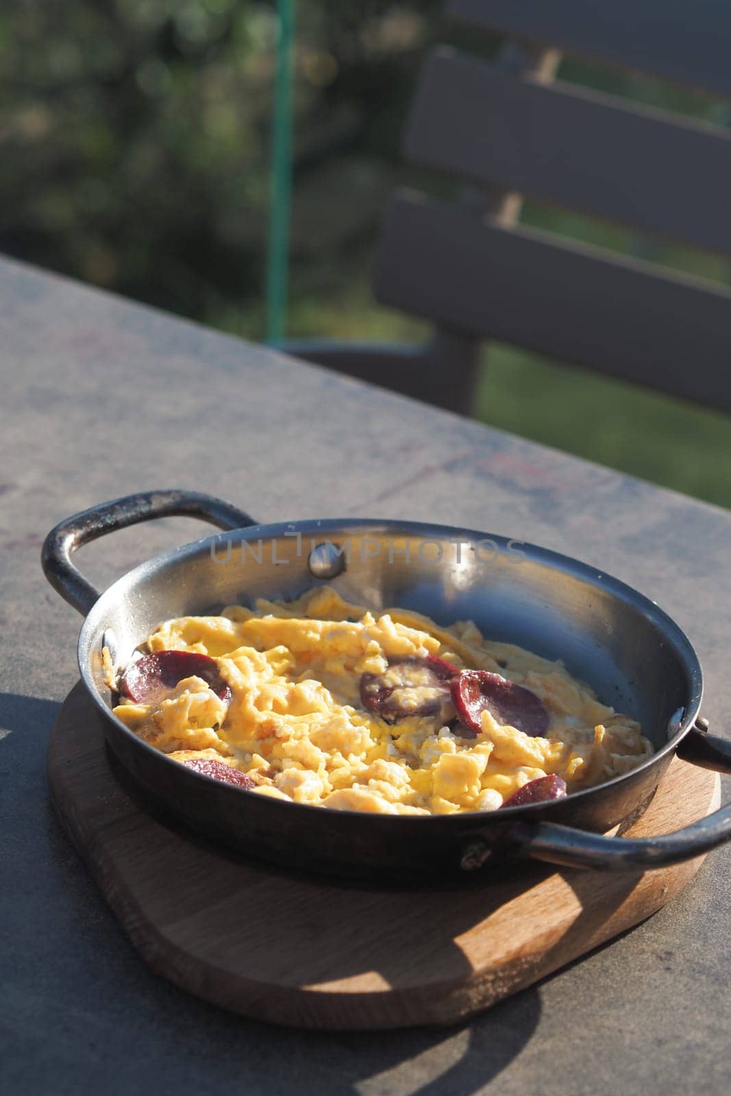 A warm skillet holds fluffy scrambled eggs with sausage, outside.