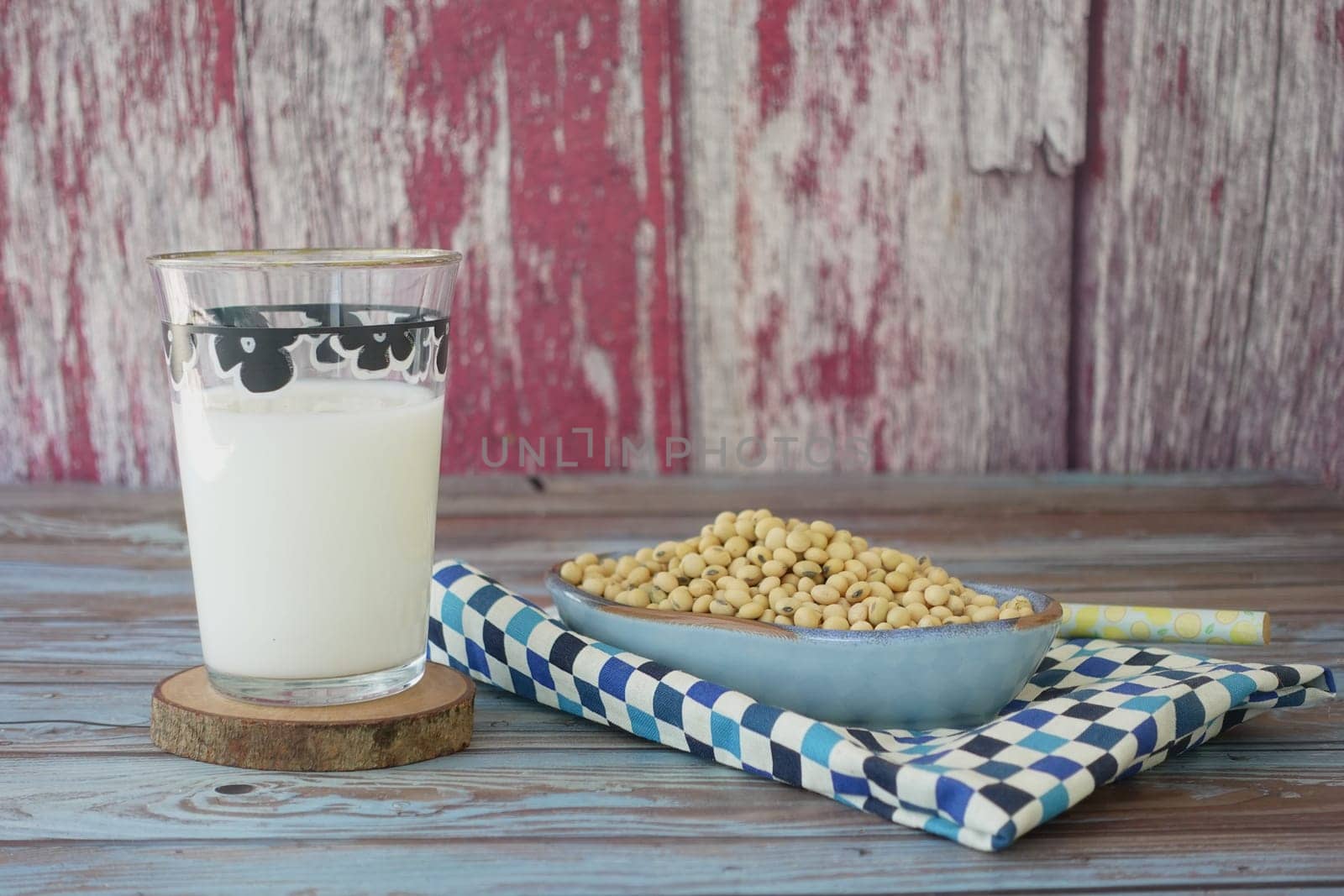 Glass of soy milk beside a bowl of raw soybeans on a colorful napkin.
