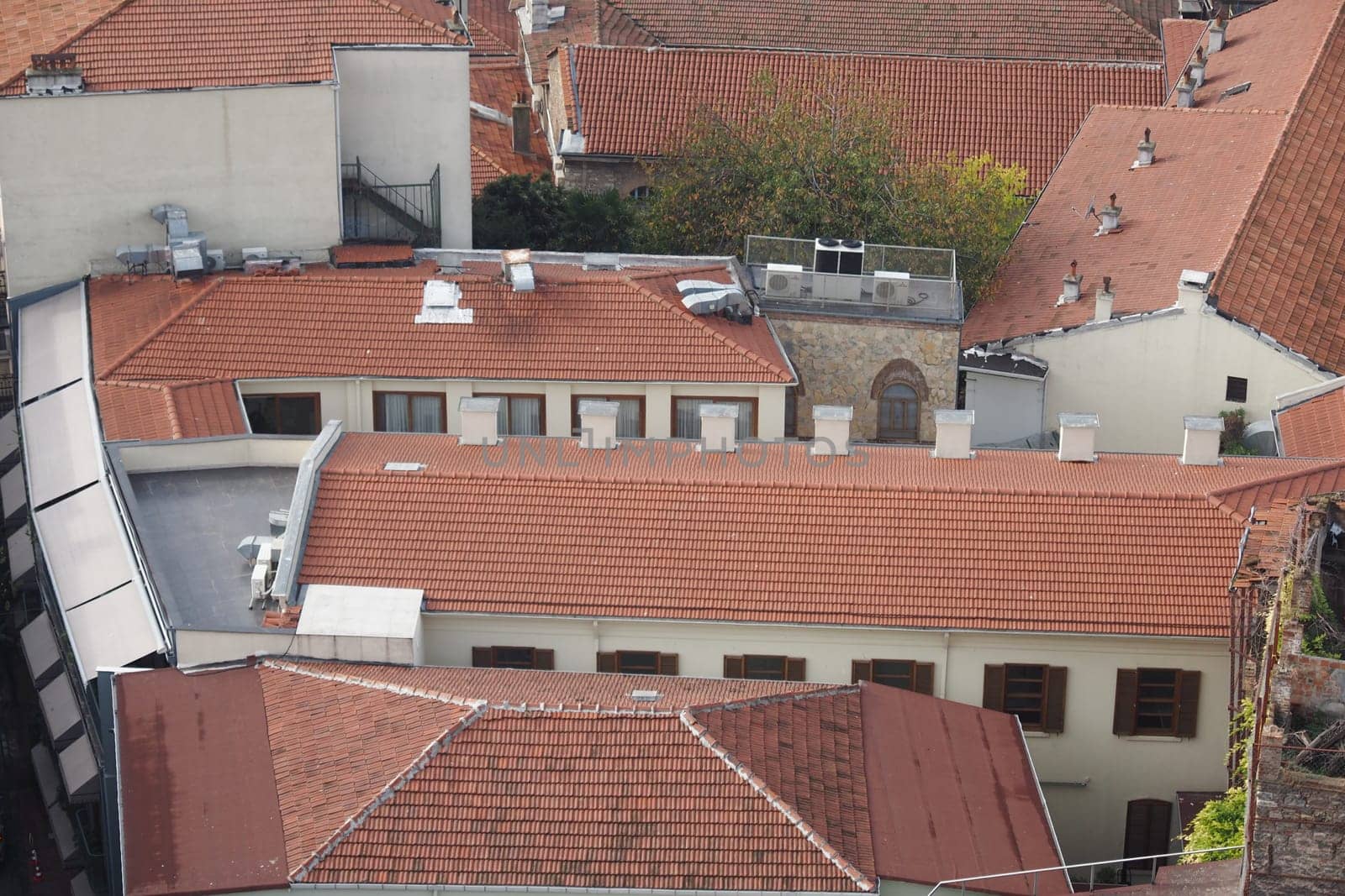 Red-tiled roofs of old buildings are viewed from above in a city.
