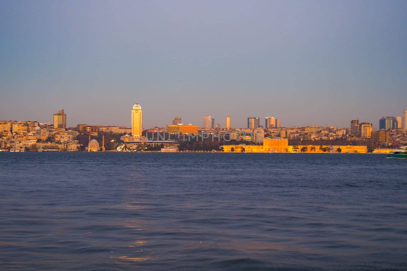 The city skyline shimmers in golden light as the sun sets over water.