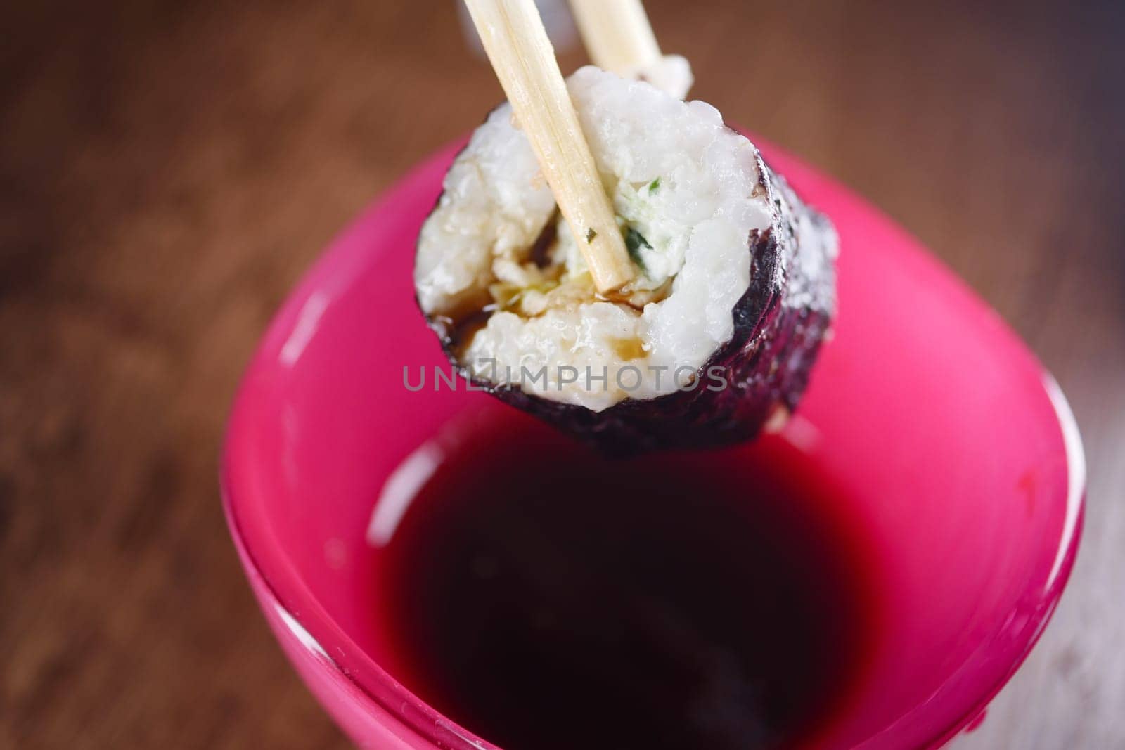 A sushi roll is lifted with chopsticks and dipped into soy sauce.