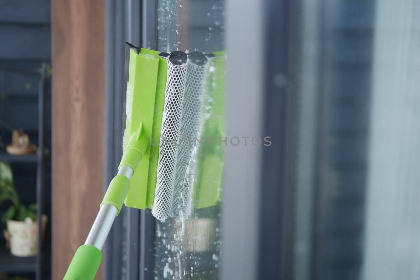 A person is cleaning a glass window using a squeegee tool indoors.