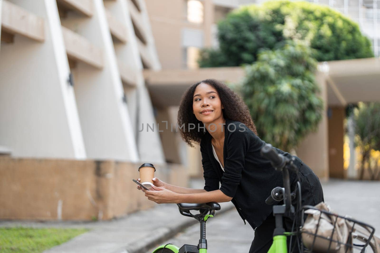 Focused on her sustainable living goals, this woman enjoys a coffee break, leaning on her vibrant green bicycle amidst an urban backdrop, connecting with her city.
