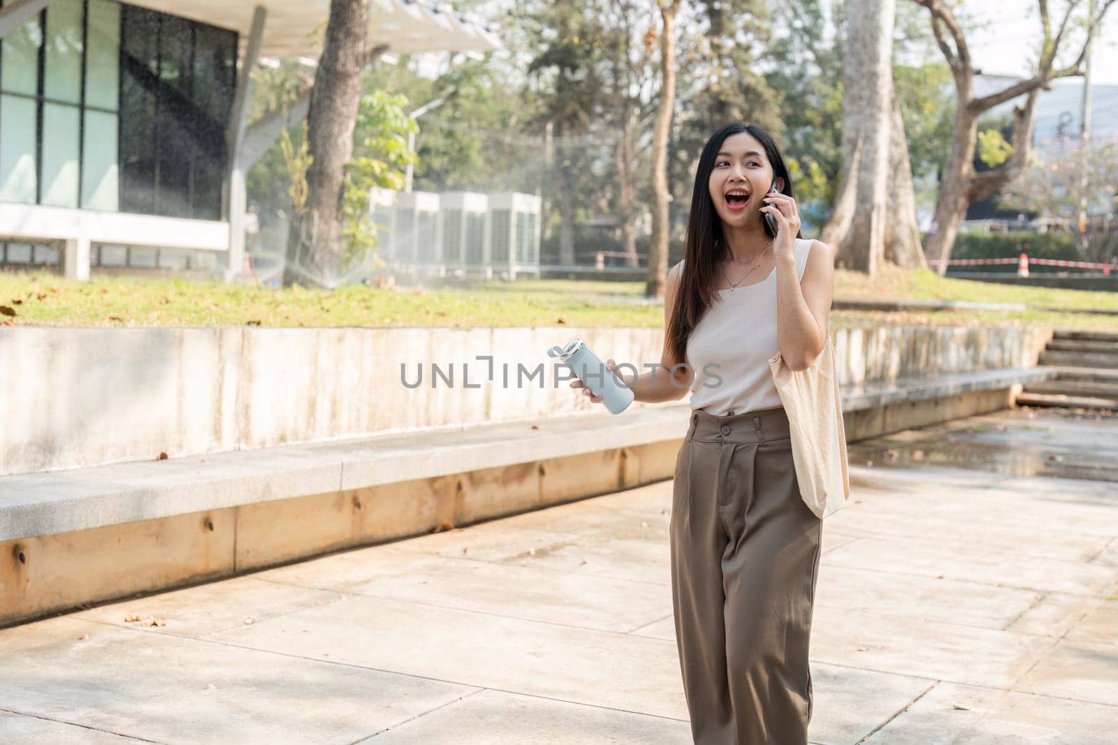 A young woman walks with excitement while talking on her phone, showcasing her commitment to a sustainable lifestyle.