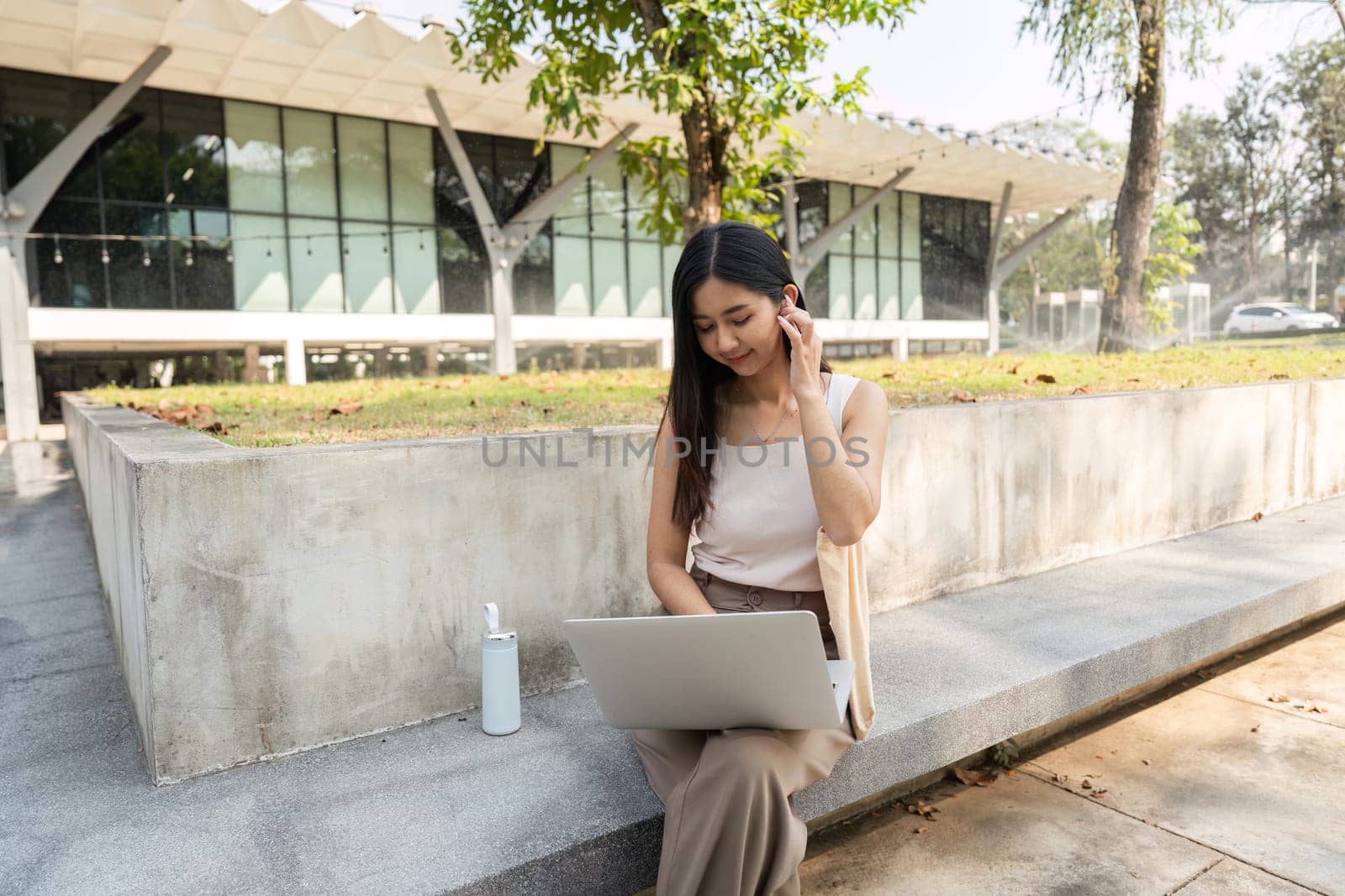 A young woman focuses on her laptop in a beautiful outdoor environment, embodying a sustainable lifestyle with her reusable items.