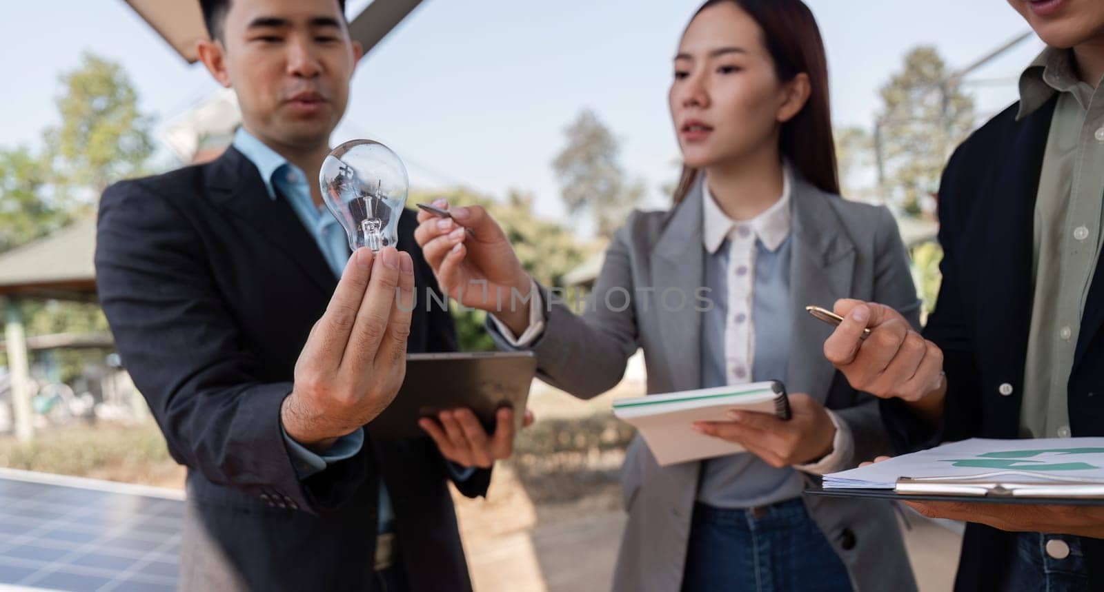 A team of professionals engaging in a discussion about sustainable energy solutions while holding innovative light bulb technology, emphasizing collaboration and green business practices.